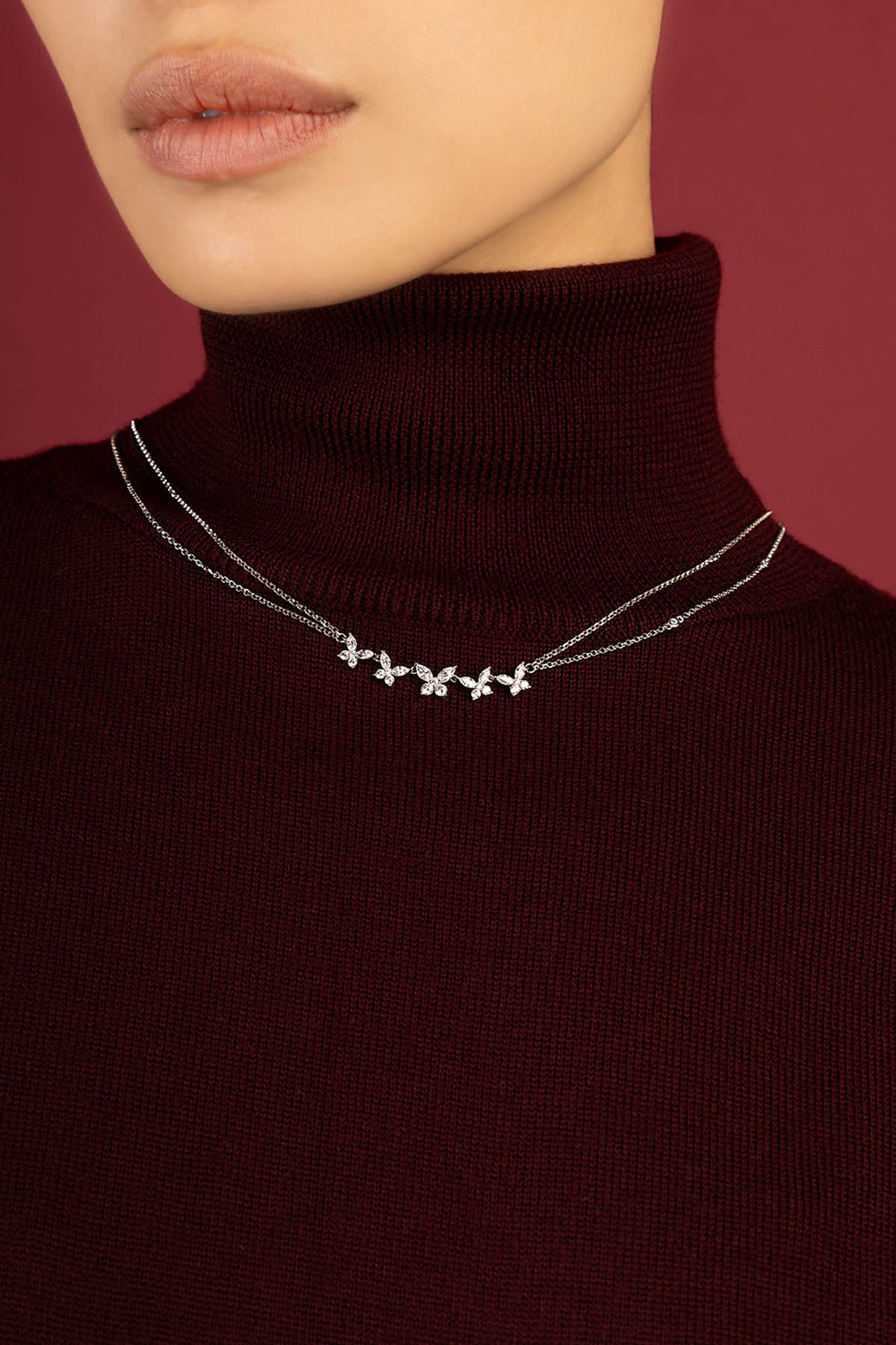 Woman wearing APM double-chain necklace, delicate floral shimmer against deep burgundy.