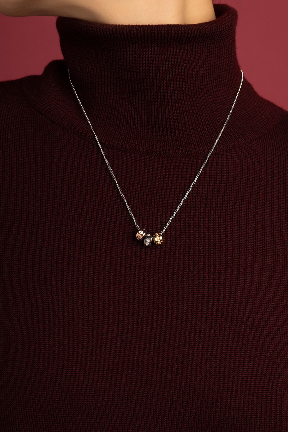 Woman wearing APM Monaco necklace, three tricolor charms whispering quiet elegance.