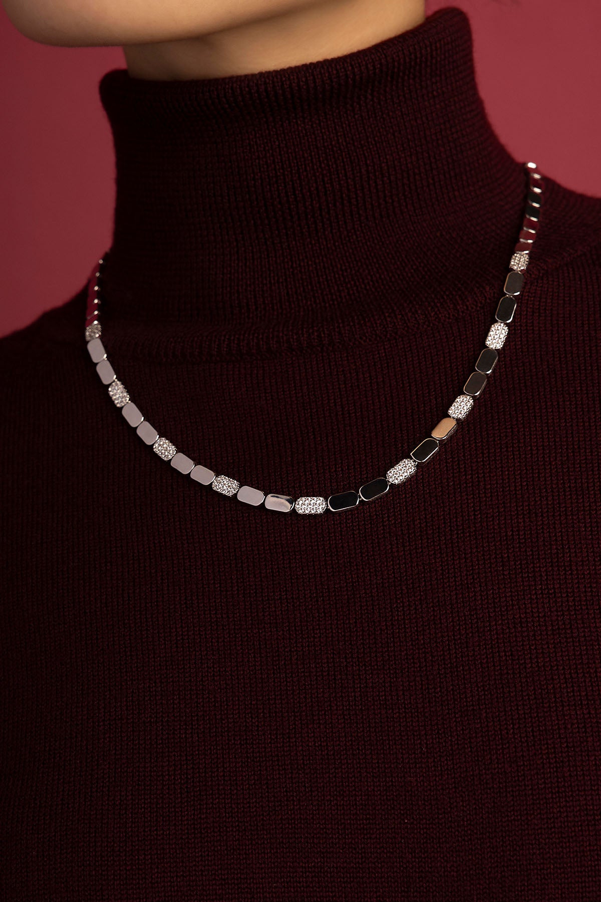 Woman wearing APM Monaco necklace, a modern rhythm of shimmer against burgundy.