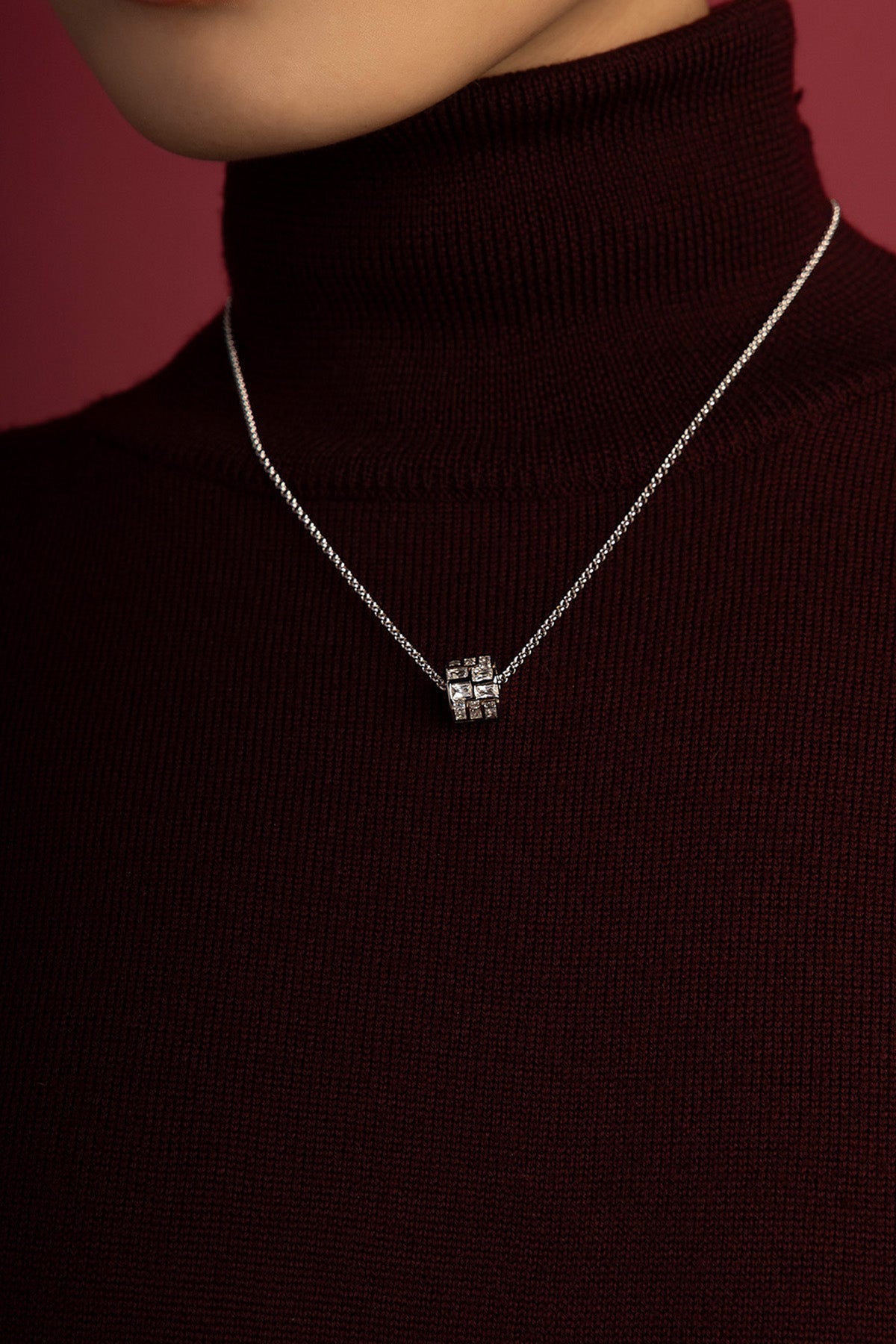 Woman wearing APM Monaco necklace, a luminous cube pendant glowing against burgundy.