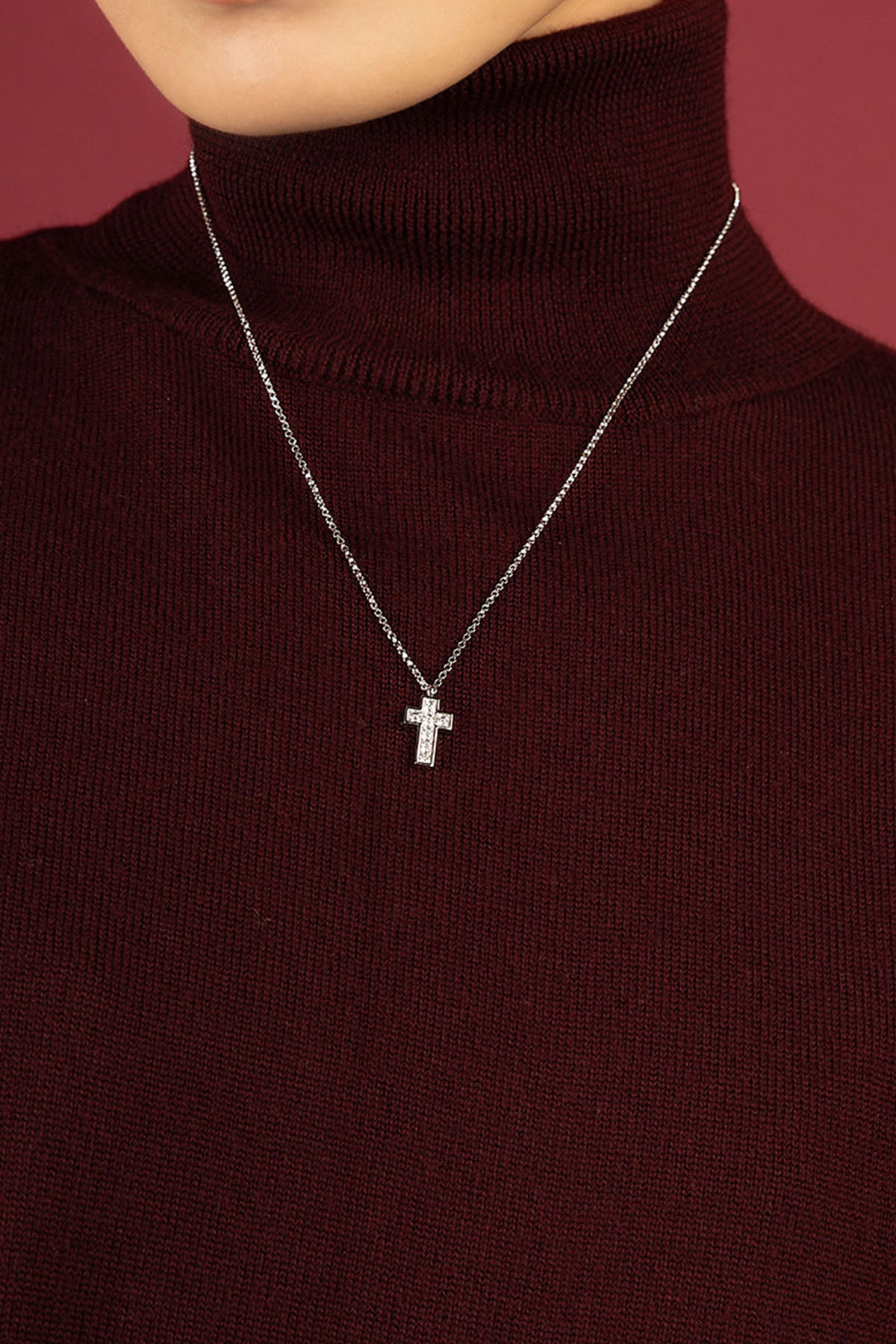 Woman wearing APM cross necklace, a delicate sparkle on cozy burgundy knit.