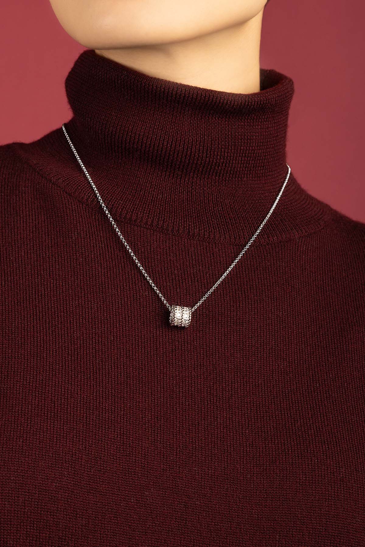 Woman wearing APM Necklace, a quiet sparkle against burgundy warmth.