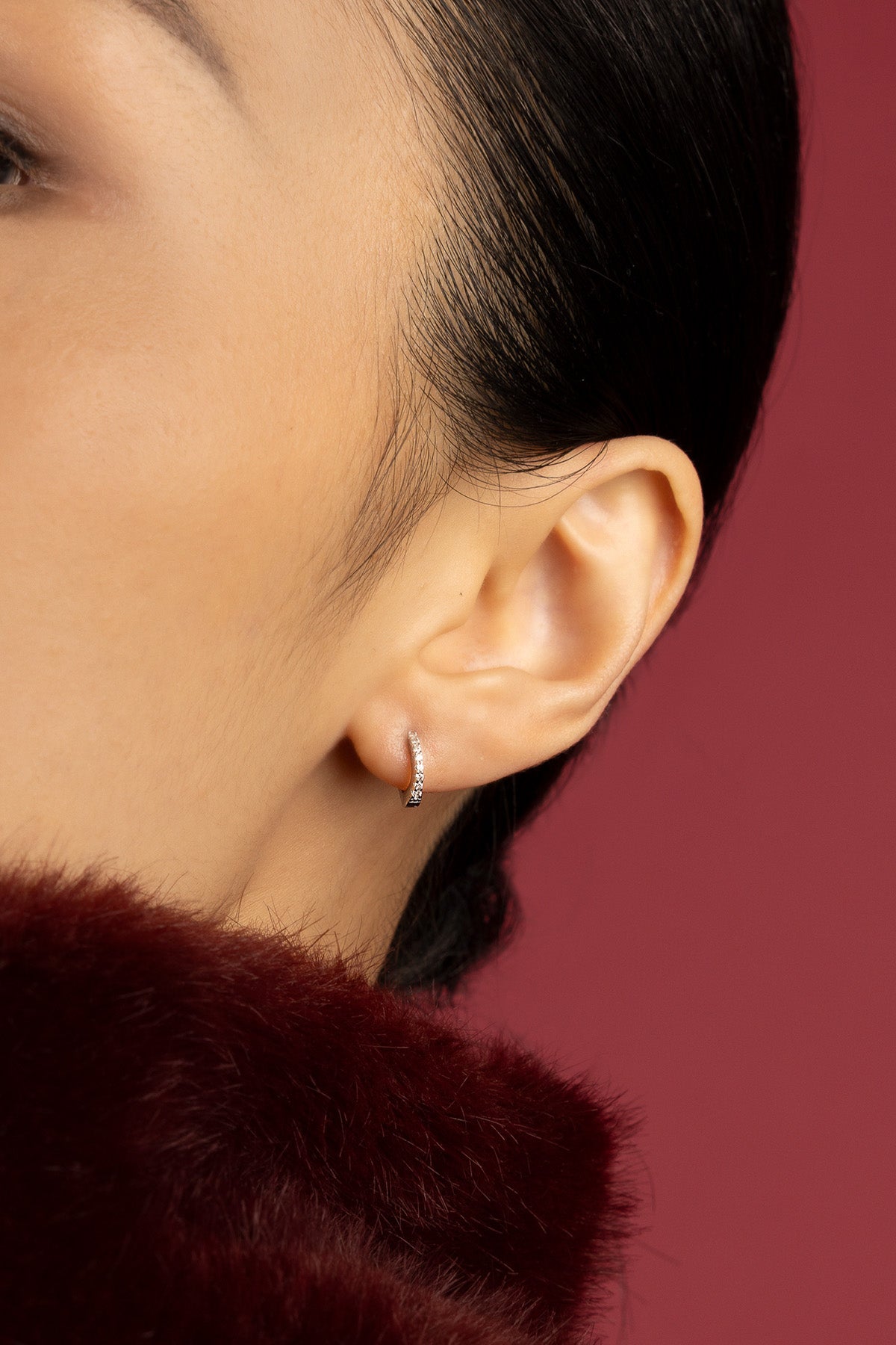 Woman wearing APM Monaco hoop earring, a delicate shimmer against burgundy elegance.