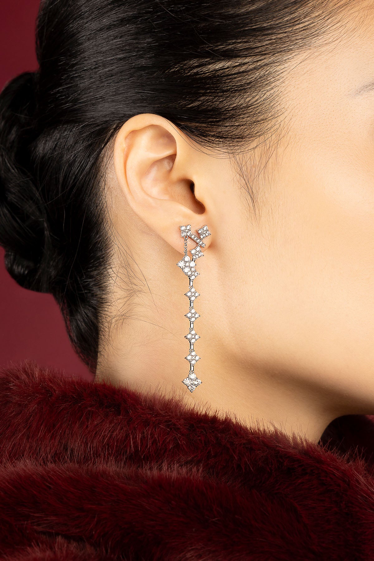 Woman wearing APM drop earrings, a cascade of starlit elegance against crimson.