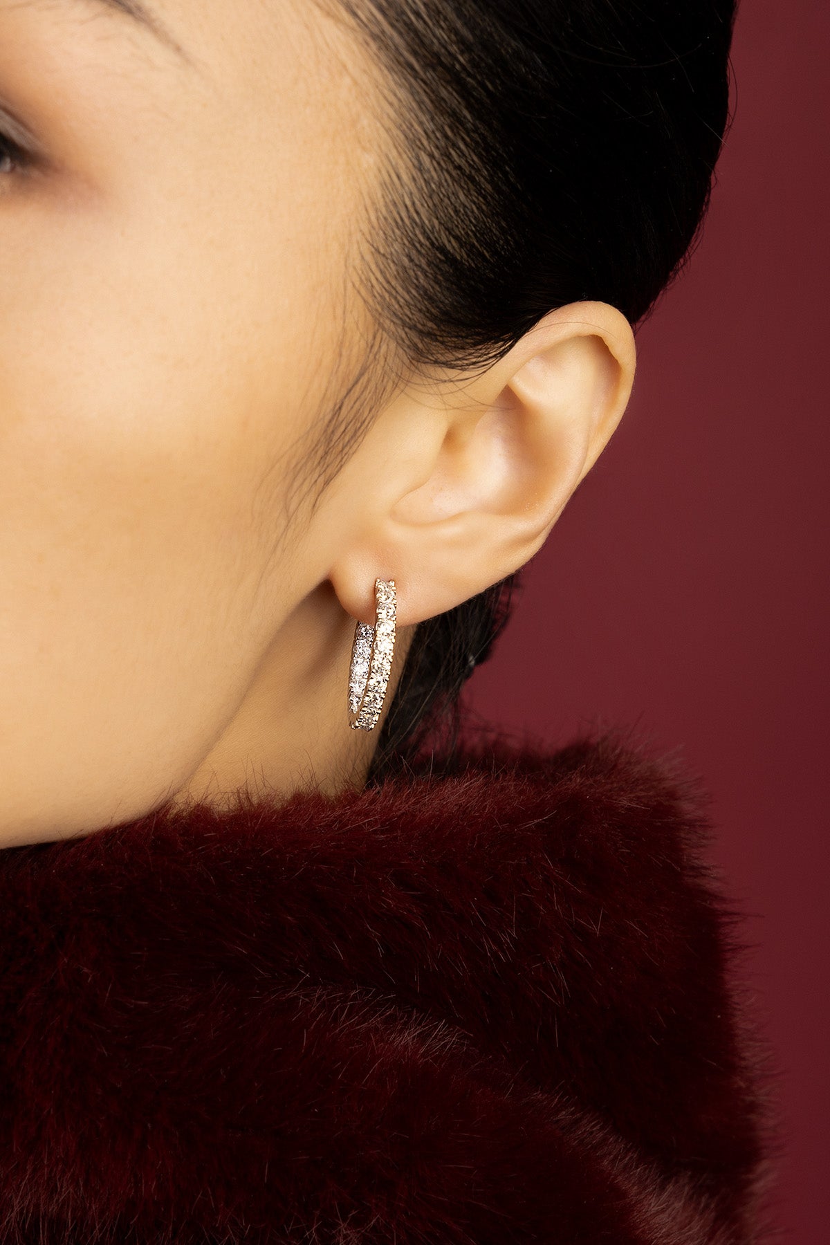 Woman wearing APM hoop earrings, a sparkling whisper against burgundy warmth.