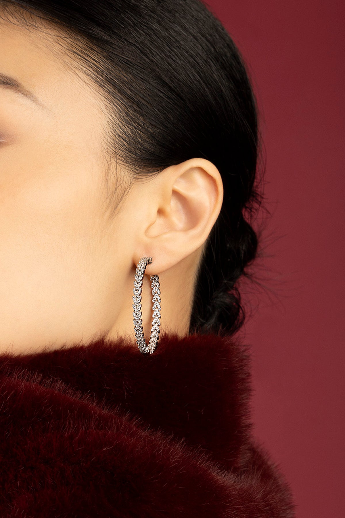 Woman wearing APM hoop earrings, a sparkling statement against deep burgundy elegance.
