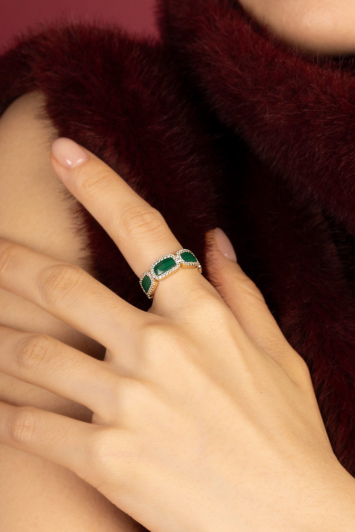 Woman wearing APM Monaco ring, green stones glowing against velvety winter warmth.