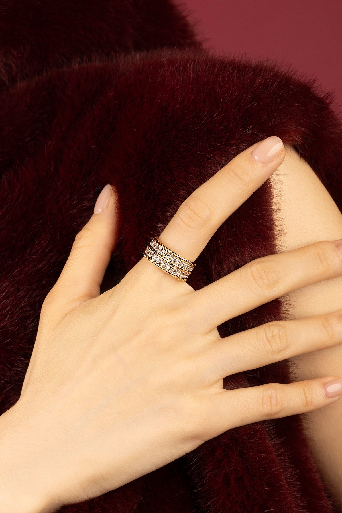 Woman wearing APM Ring, a golden shimmer against plush burgundy elegance.