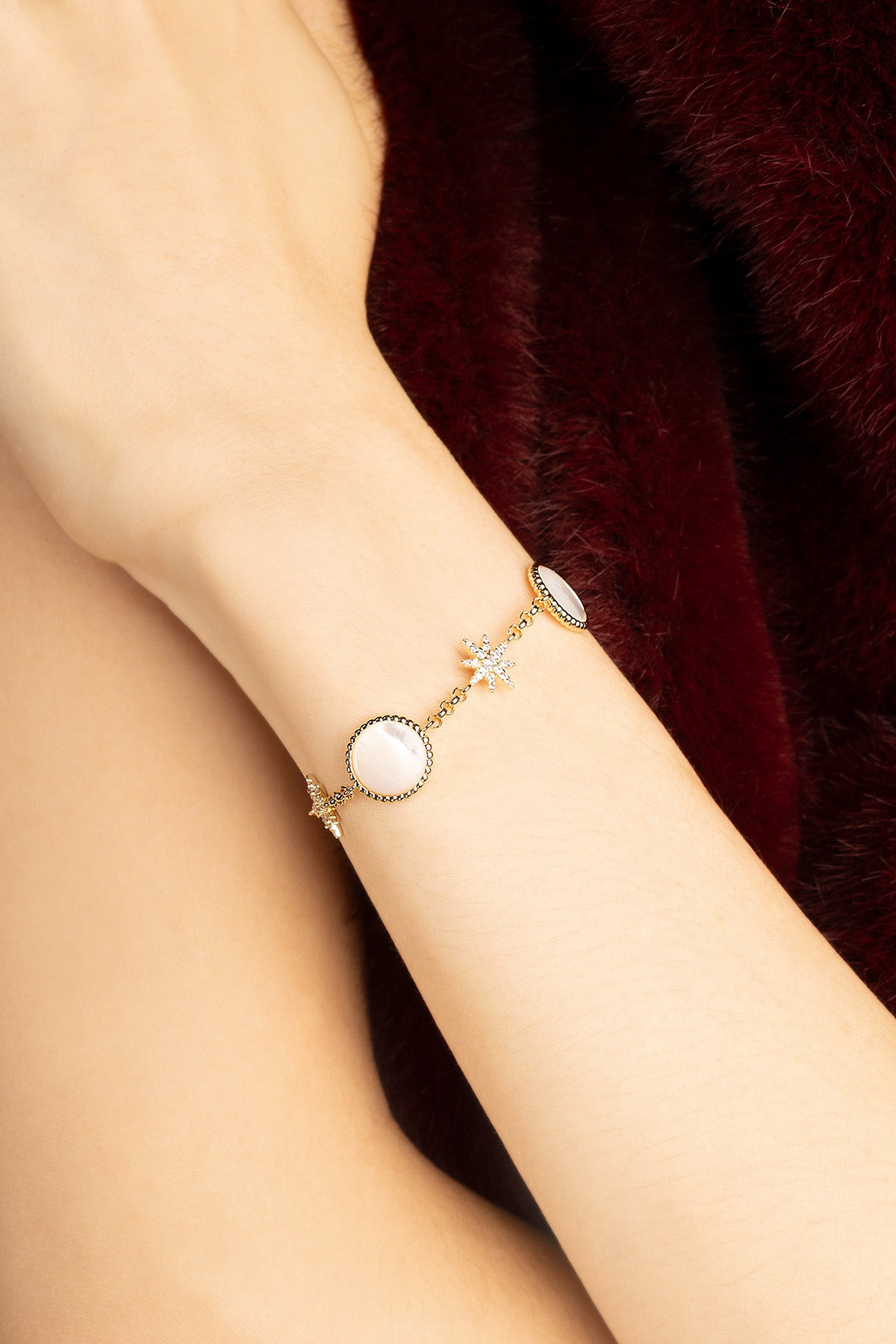 Woman wearing APM Monaco bracelet, a celestial whisper against burgundy warmth.