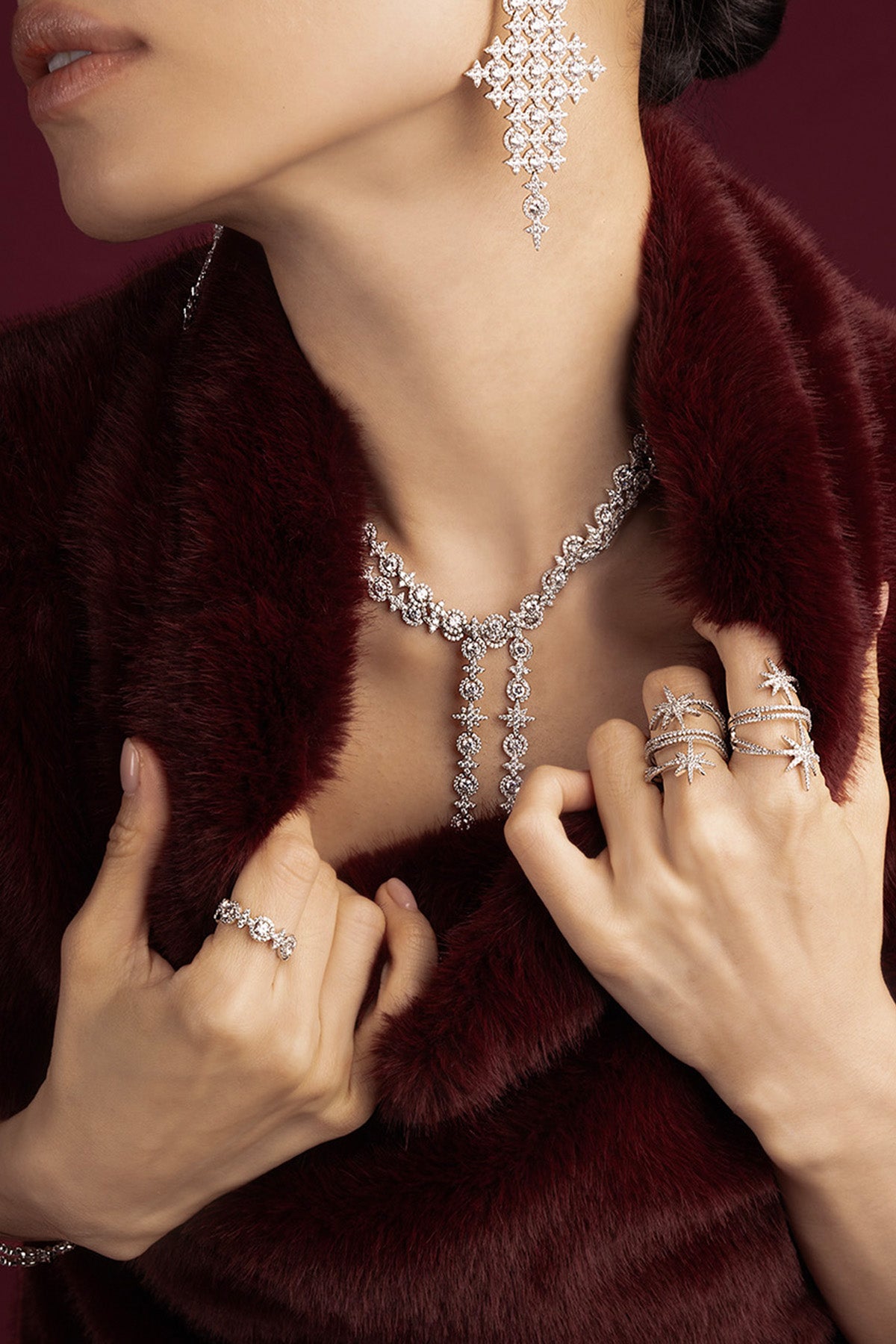 Woman wearing APM necklace, earrings and rings, a shimmering cascade against burgundy elegance.