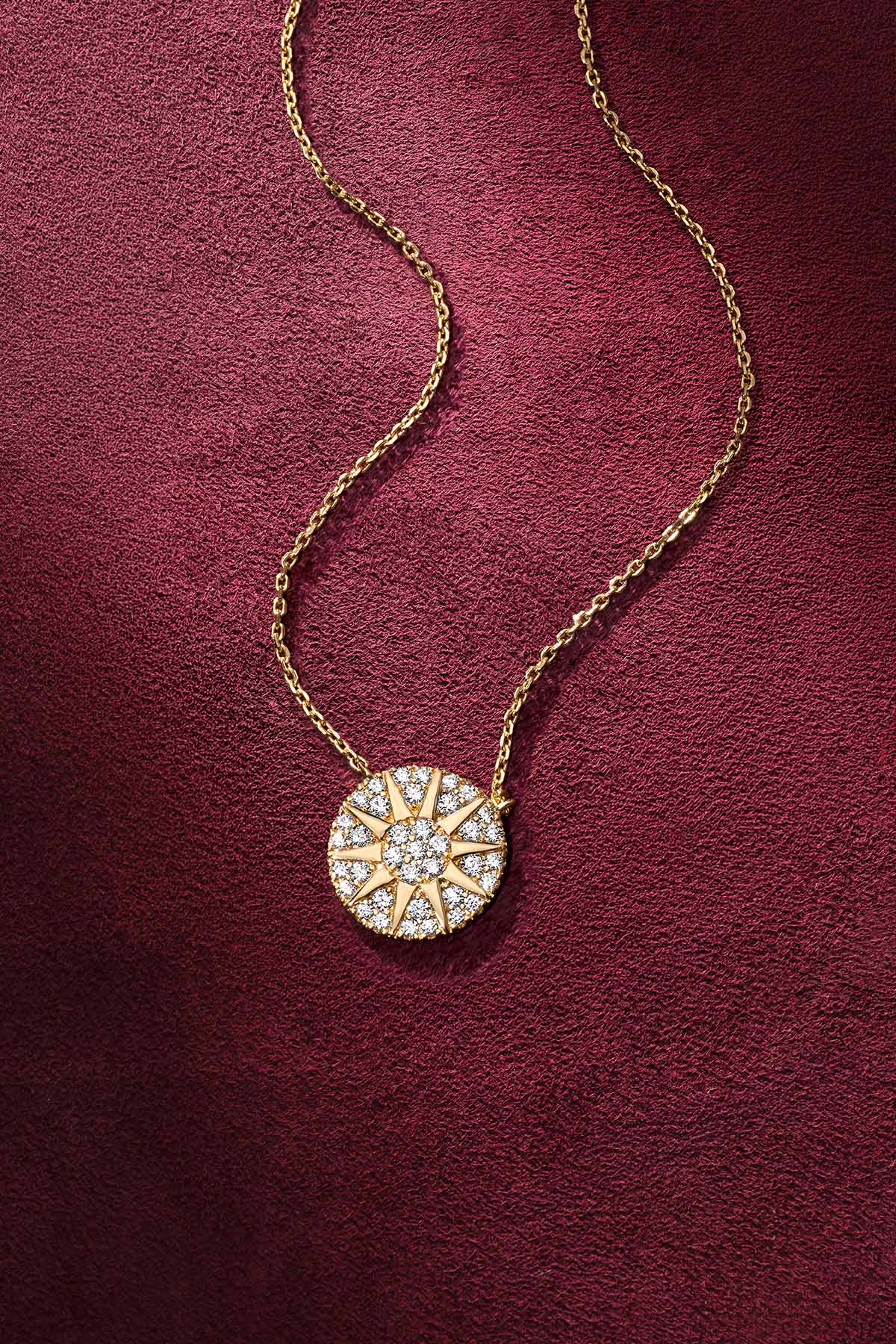 APM Necklace glowing in gold, a radiant sun on velvet burgundy.