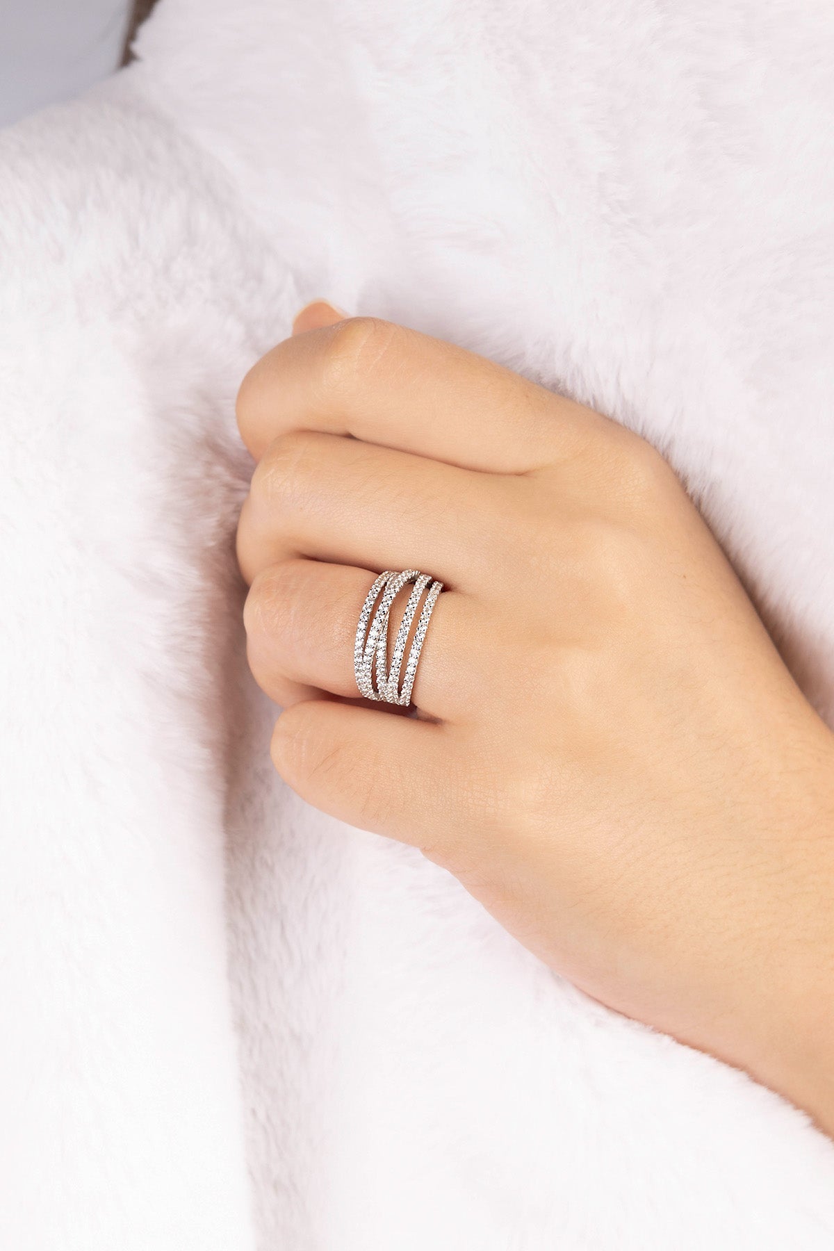 Hand wearing multiple APM MONACO silver rings with five-hoop design on a white background