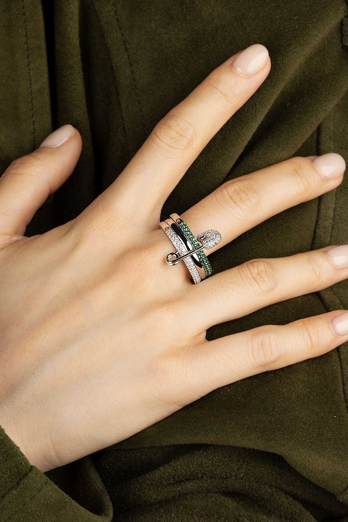 Hand wearing multiple rings with green stones against a dark background