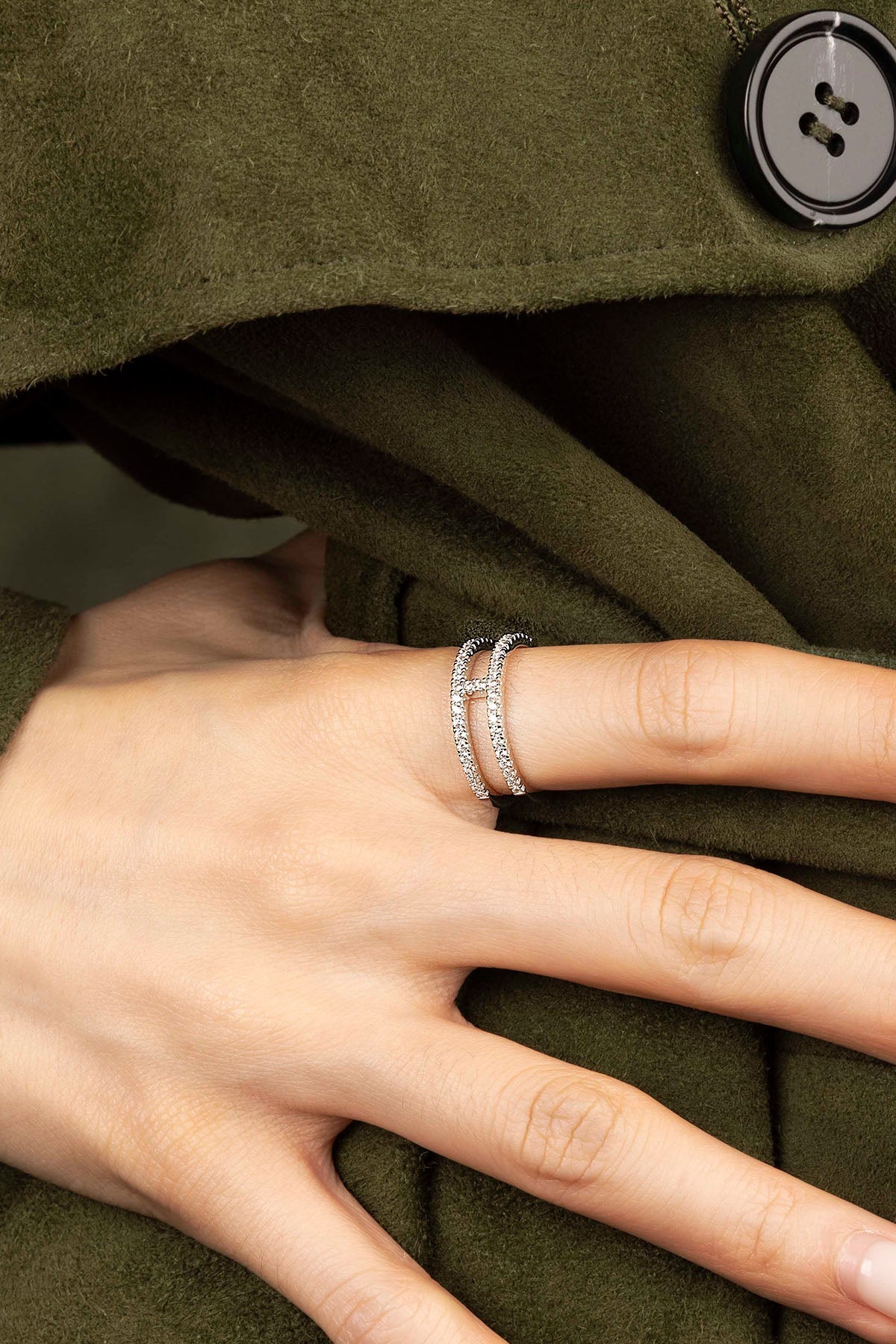 Hand wearing a silver ring on a green coat background