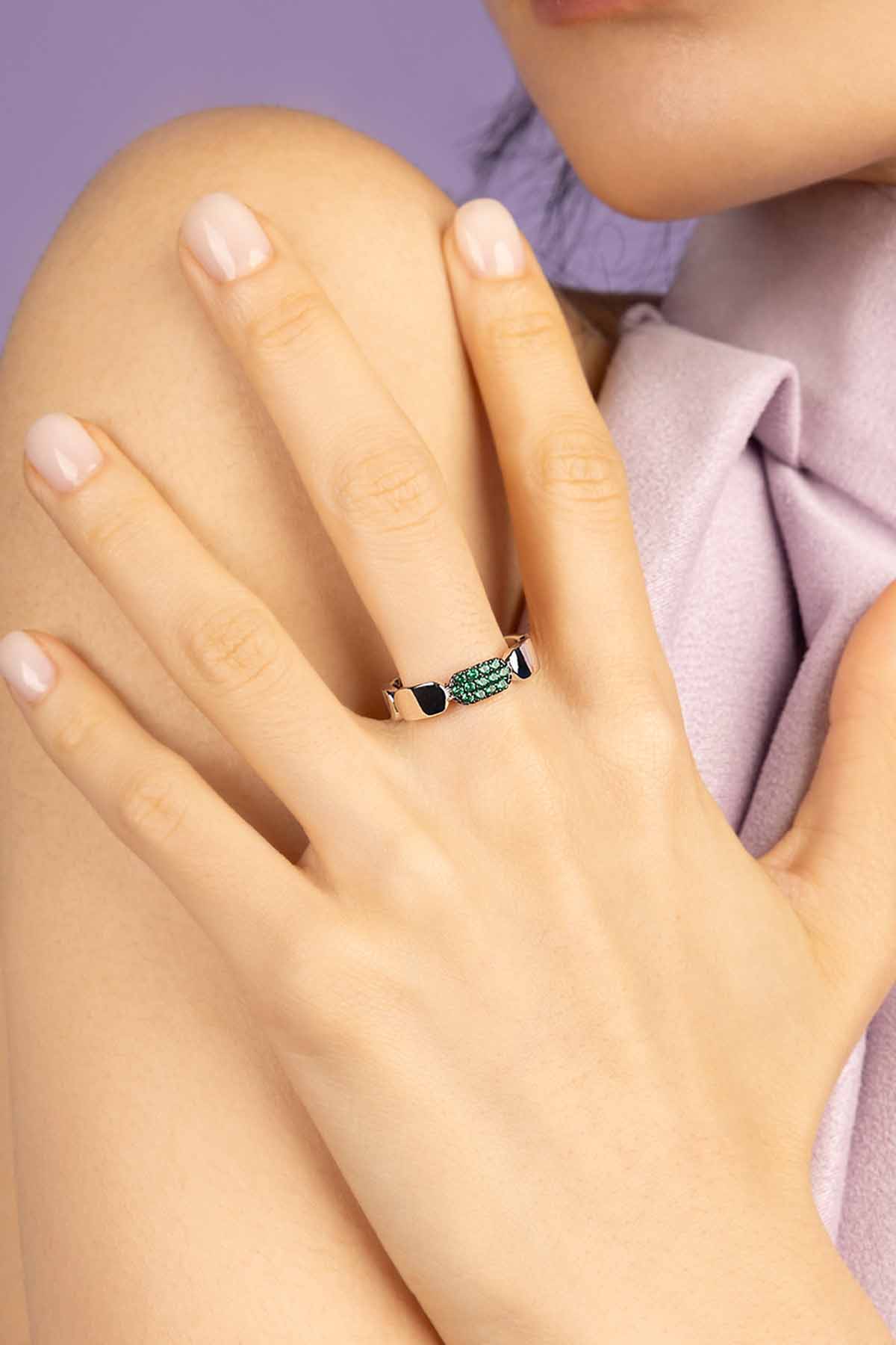 Close-up of a hand wearing an gren stones ring with a blurred background