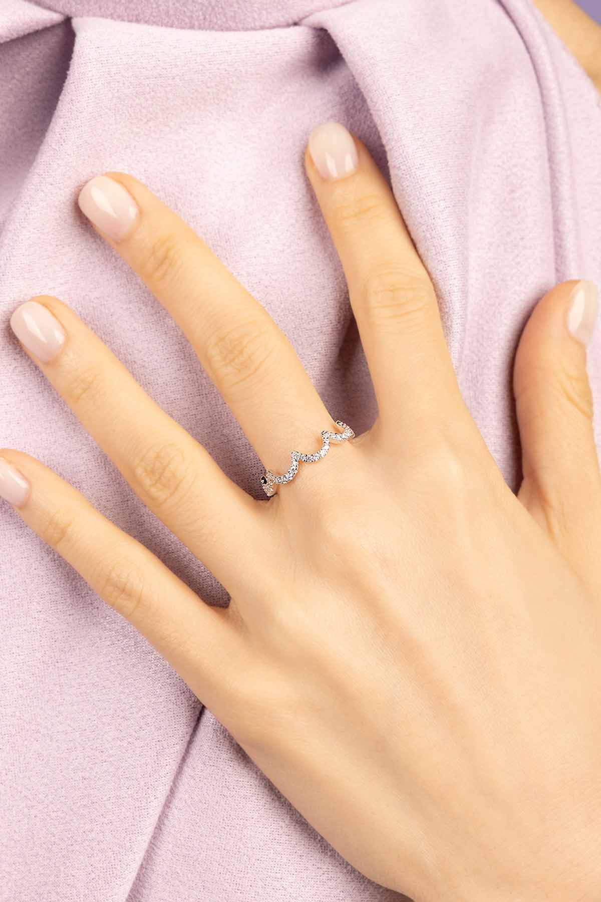 Hand wearing APM MONACO wavy silver pave ring on a soft purple fabric background