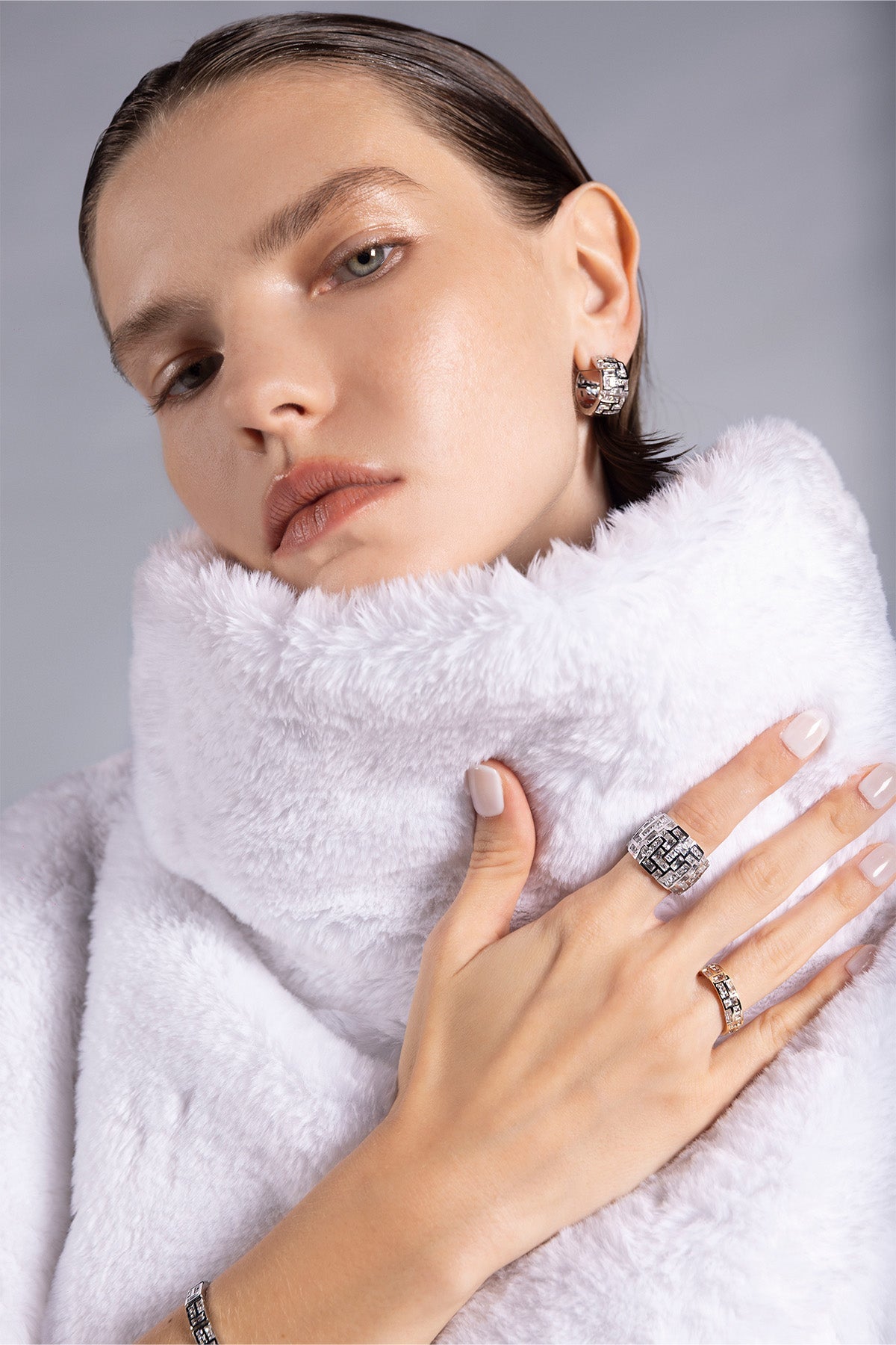 Woman wearing a white coat with close-up of APM MONACO chunky rings on a gray background