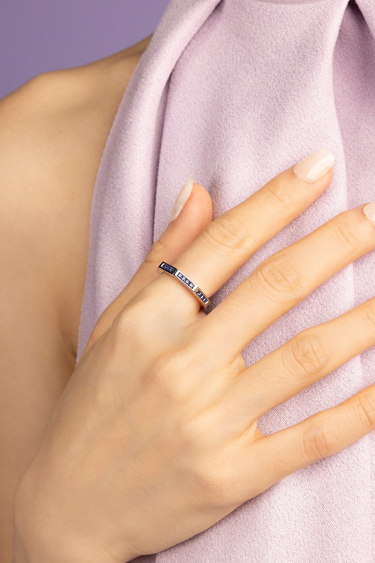 Hand wearing a ring paved with blue stones with a purple fabric background