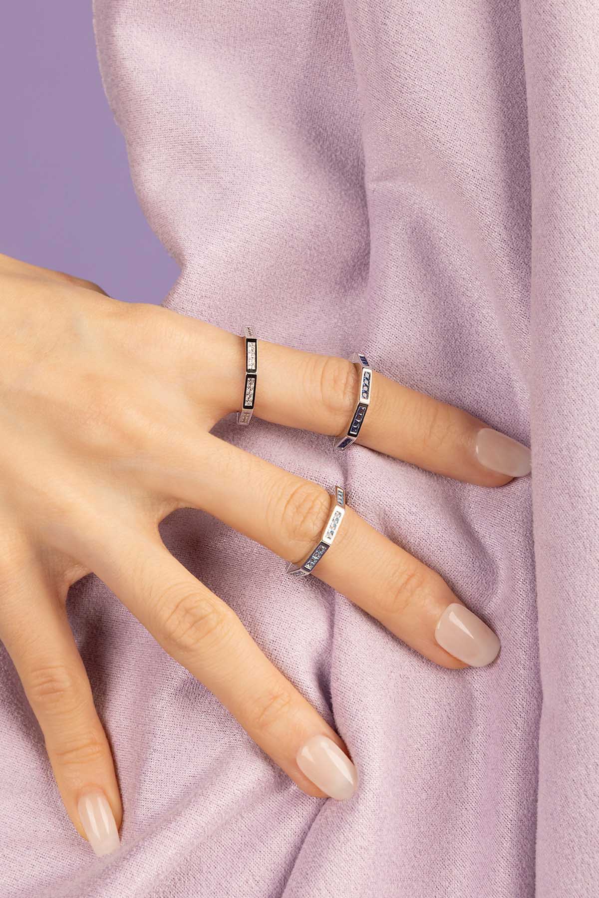 Hand wearing multiple rings on a soft pink background