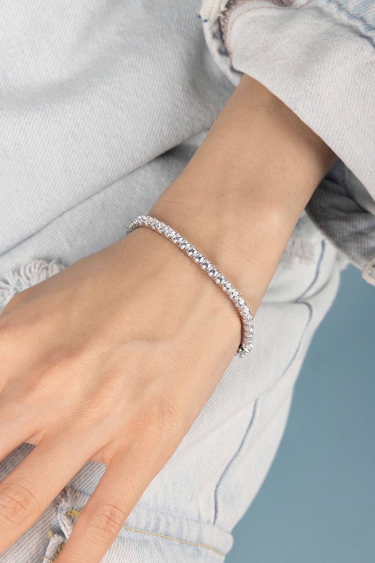 Close-up of a hand wearing a silver bracelet against a light blue background