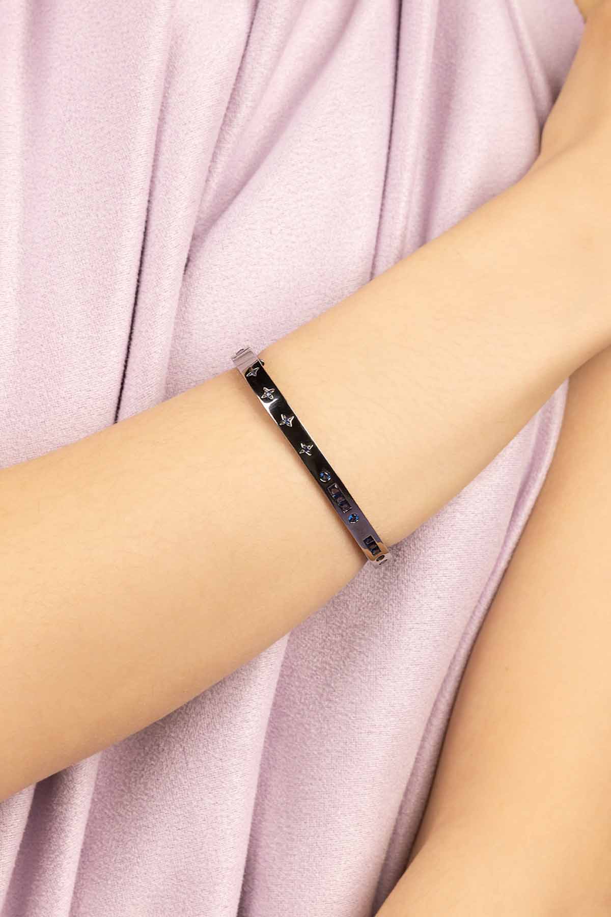 Black bracelet with white pattern on a person's wrist against a light pink fabric background