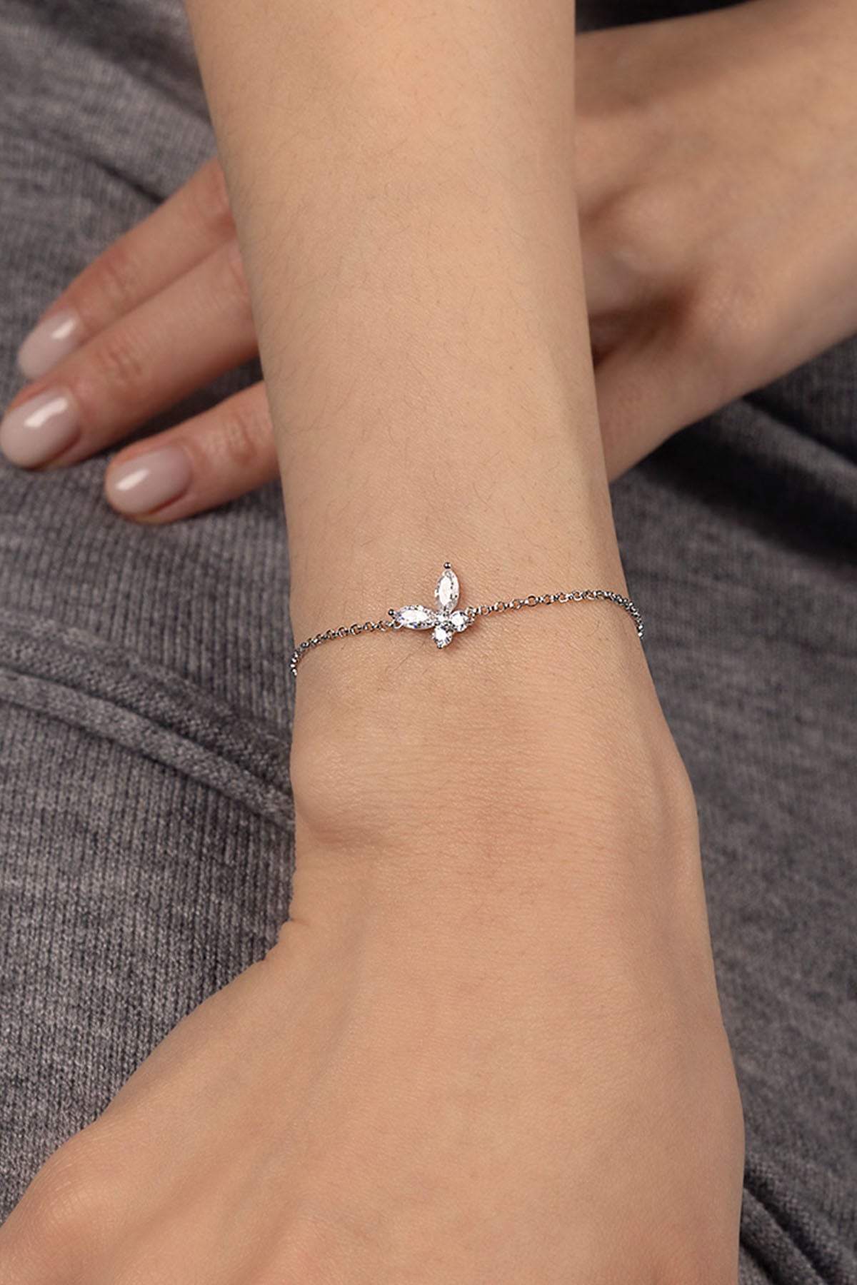 Silver bracelet with a decorative clasp on a wrist against a gray fabric background