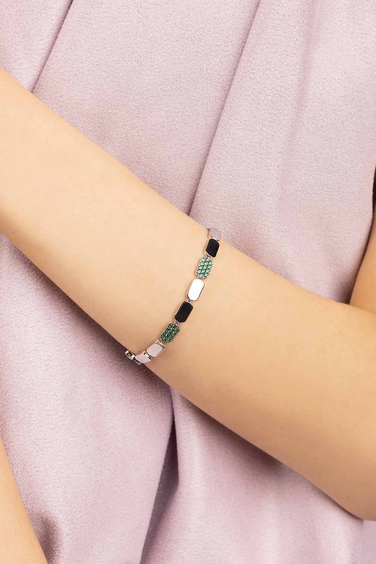 Bracelet with green stones on a person's wrist against a pink fabric background