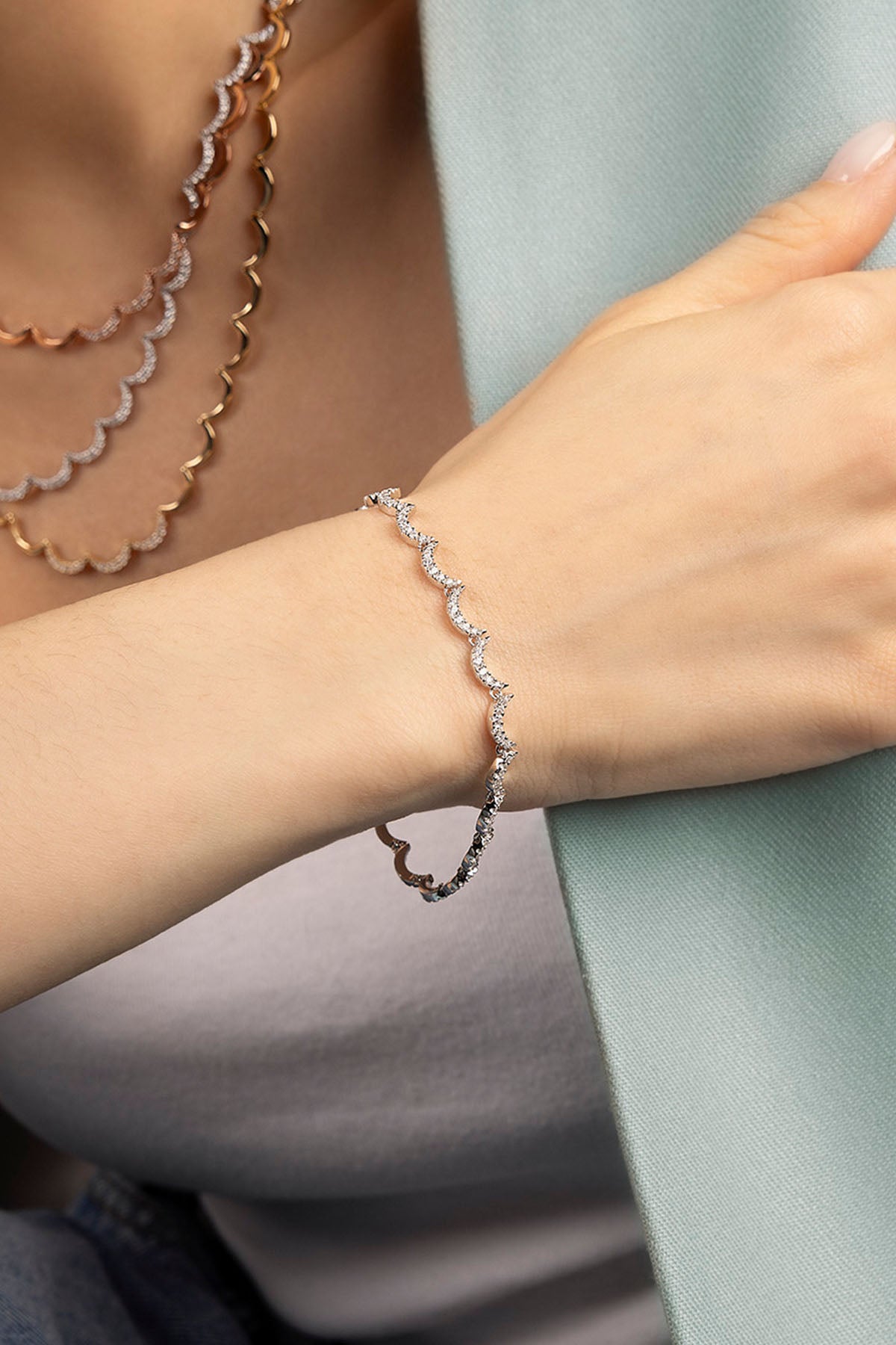 Close-up of a hand wearing a silver bracelet with layered necklaces