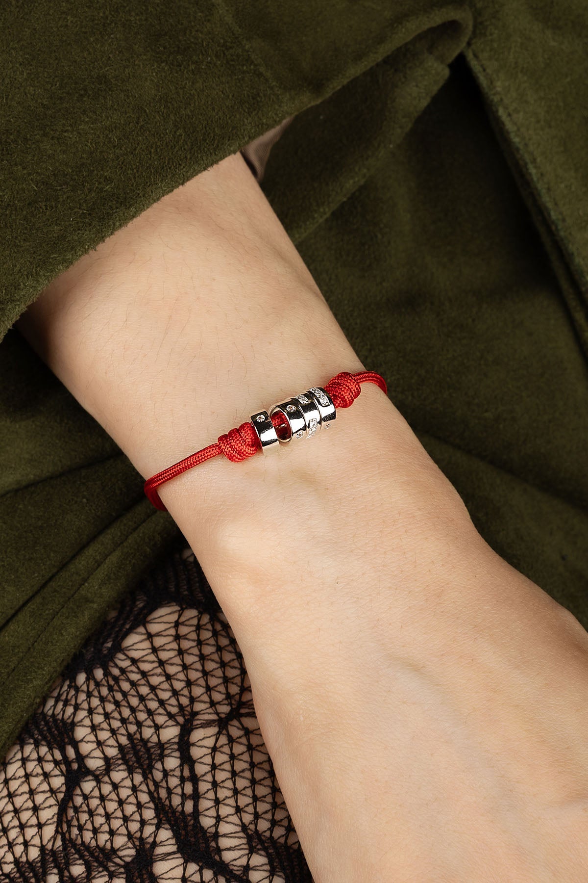 Red bracelet with silver beads on a wrist against a green fabric background