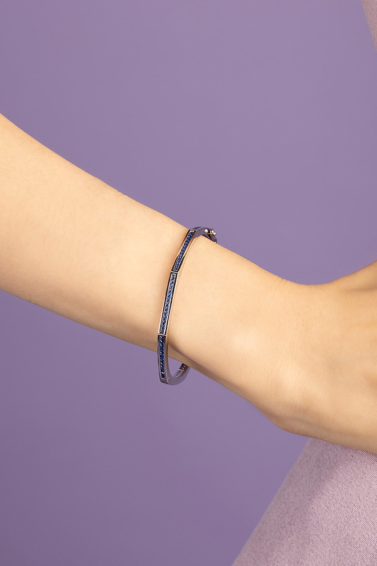 Blue bracelet on a person's wrist against a purple background