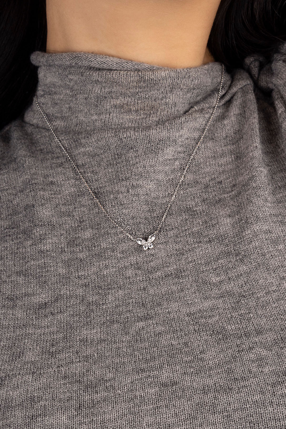 Necklace with a small pendant worn by a person in a gray sweater.