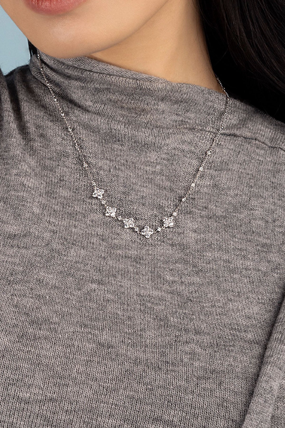 Necklace with spark pendants worn by a model in a gray sweater.