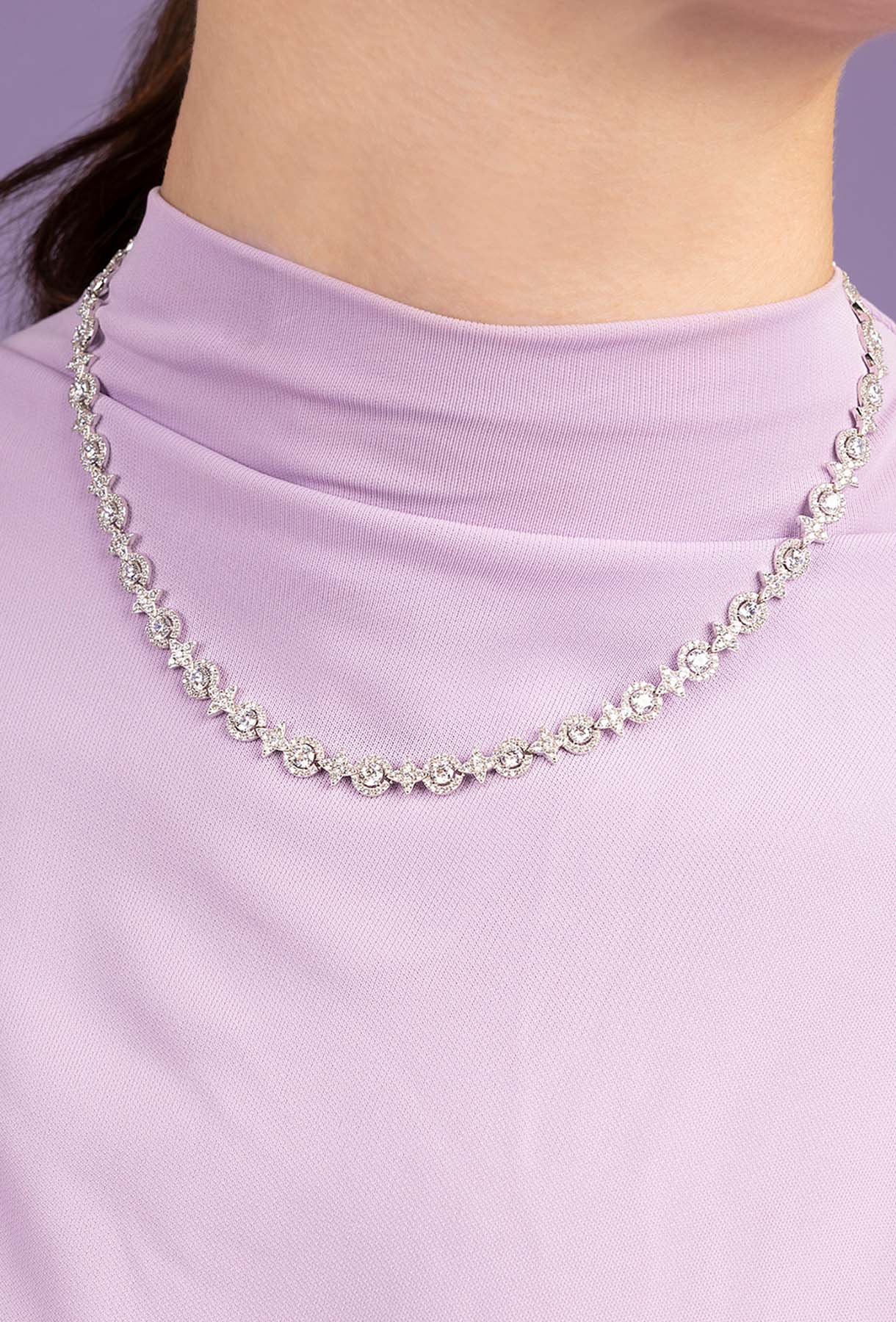 Silver necklace on a person wearing a light purple top against a solid background