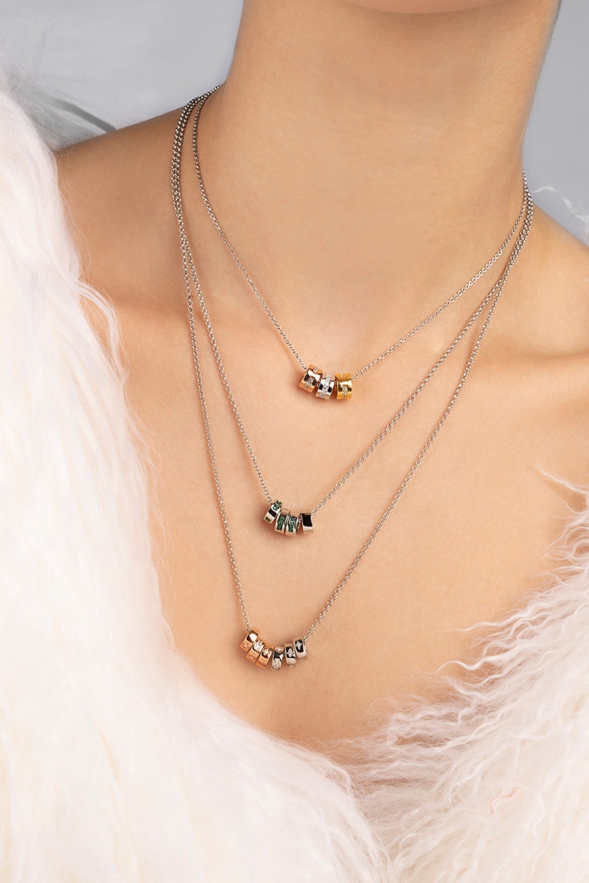 Necklaces with small pendants on a person wearing a white fur garment.