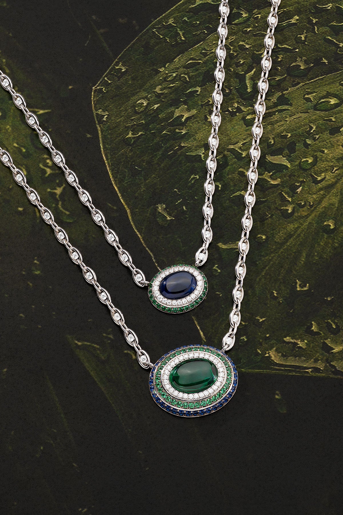 Two silver necklaces with gemstone pendants on a dark leafy background