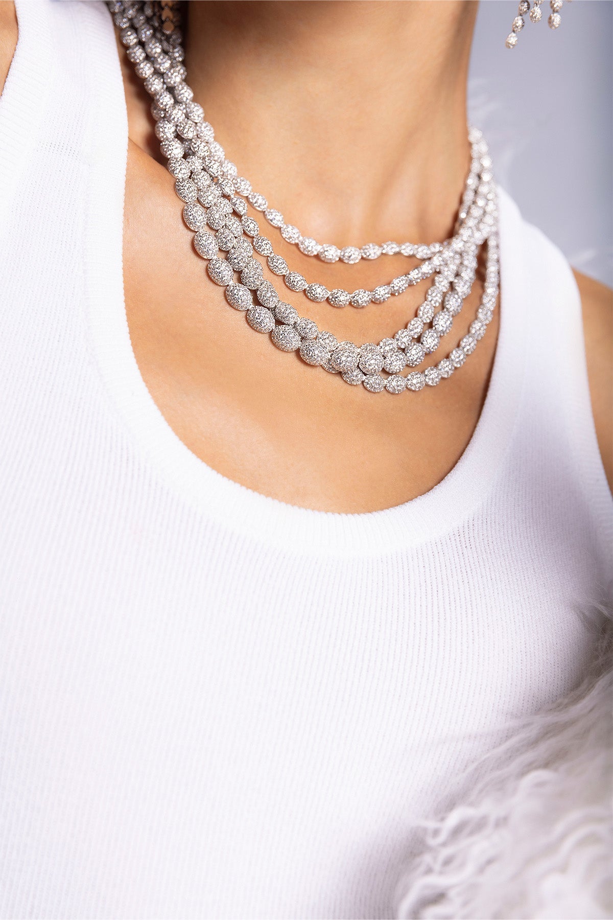 Close-up of a model wearing multiple APM MONACO pave necklaces in silver on a plain background