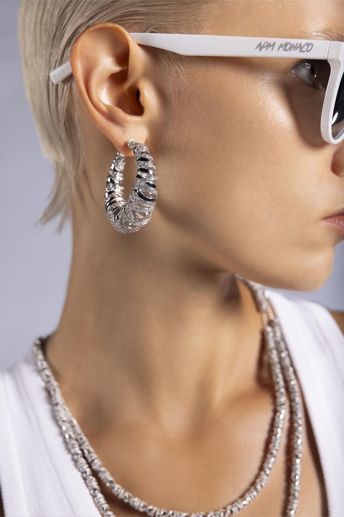 white sunglasses with APM MONACO logo and statement silver earrings worn on model
