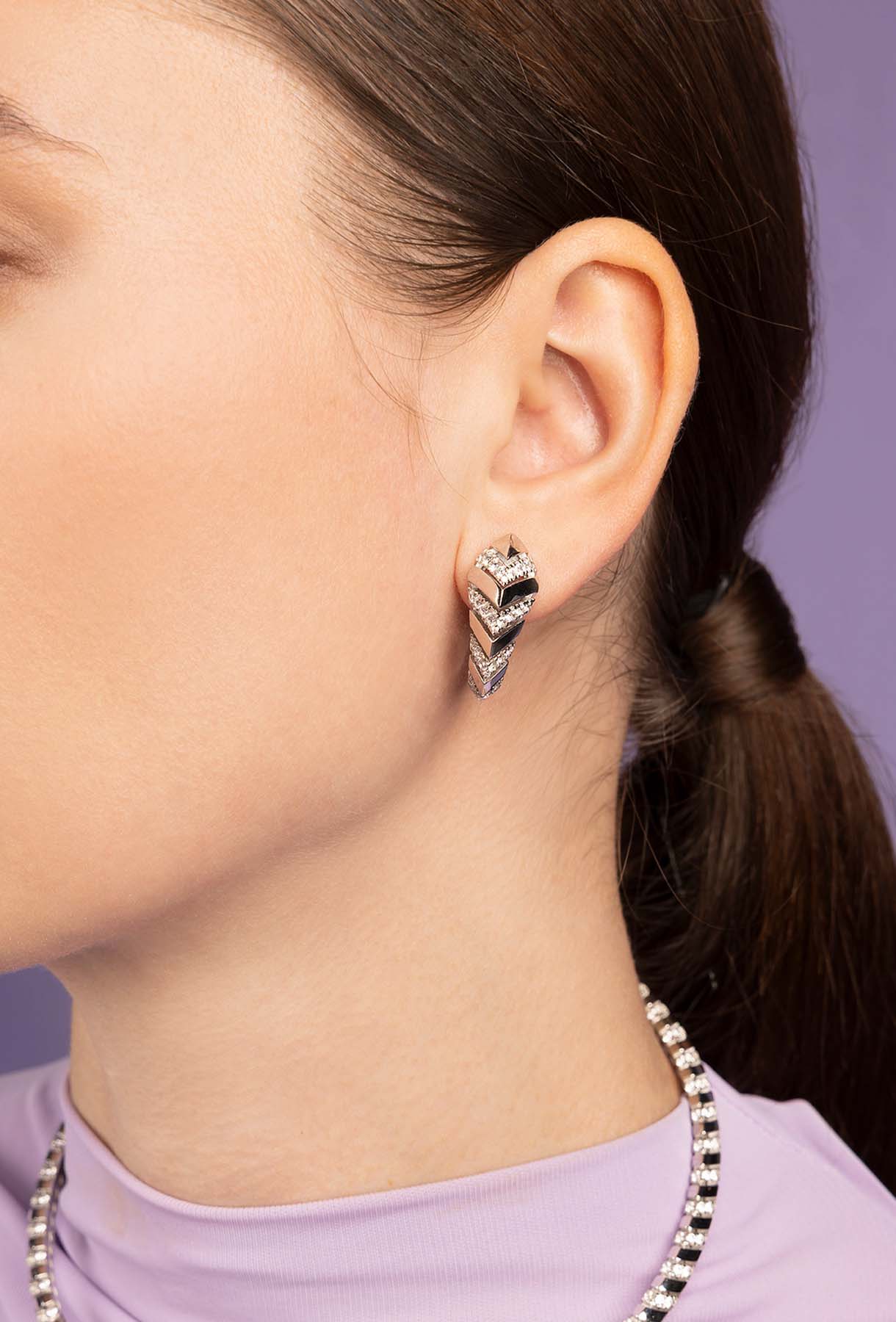 Close-up of a person wearing APM MONACO KAA Silver-tone earrings with a purple background