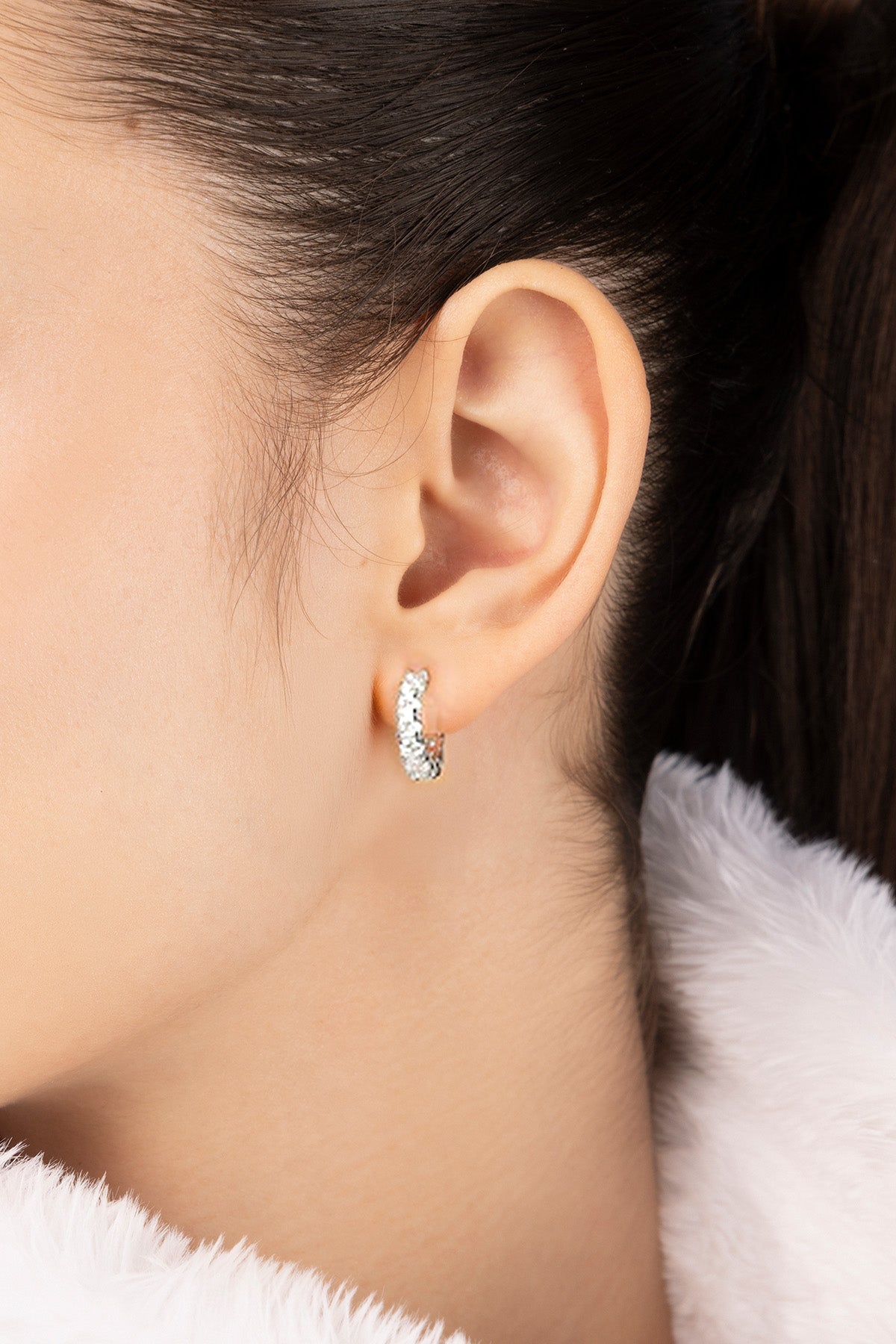Close-up of an ear wearing APM MONACO silver hoop earring with a blurred background