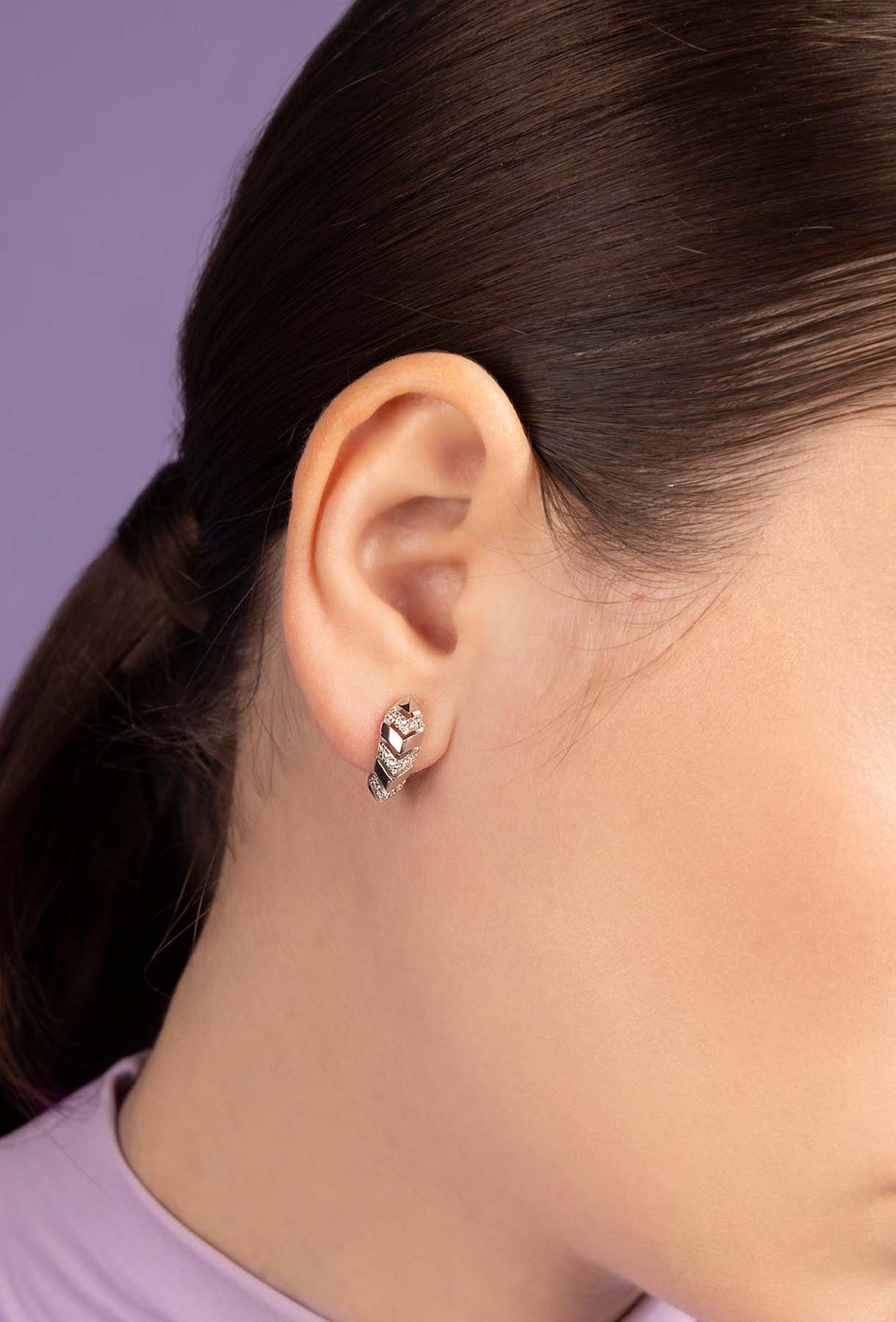 Close-up of a person wearing APM MONACO silver earring with a black design on a light purple background