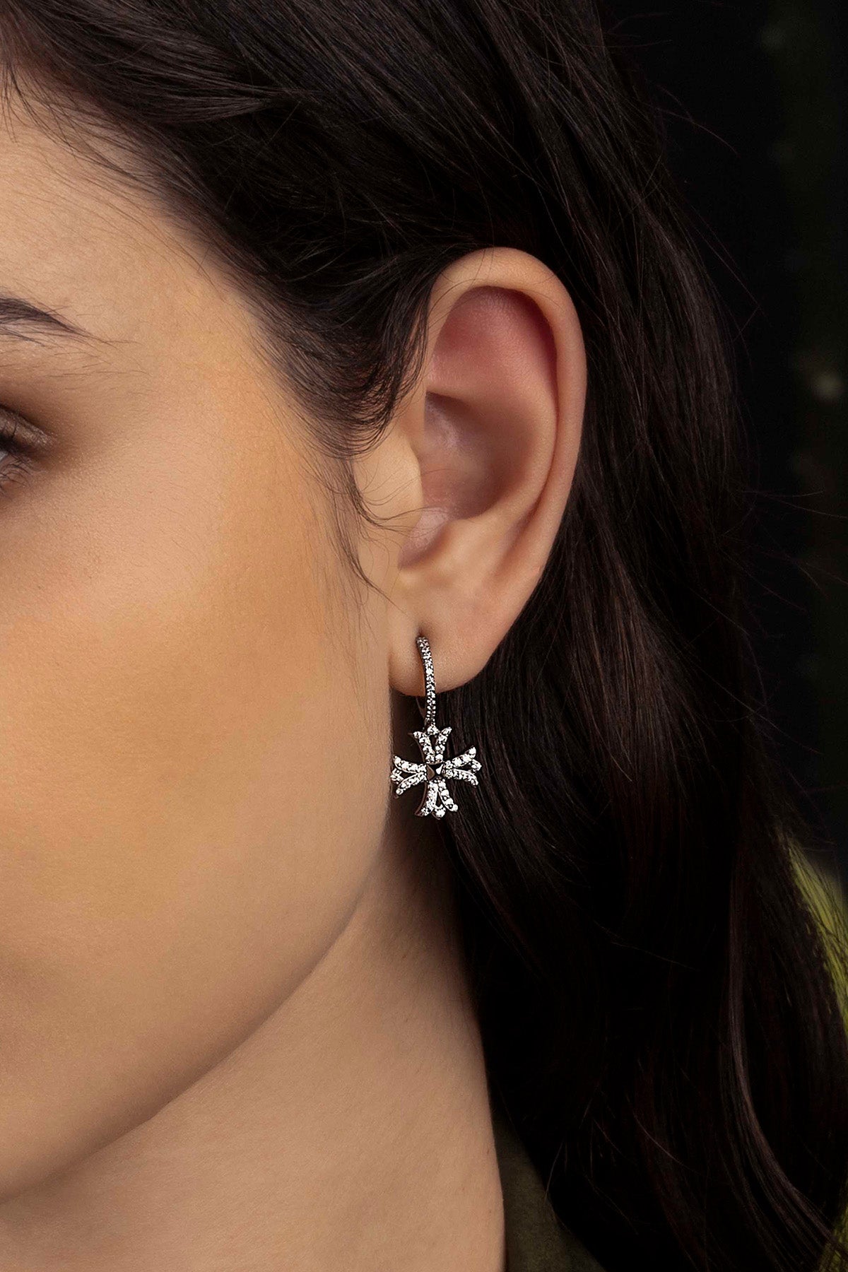 Close-up of a woman wearing a silver  earring against a dark background