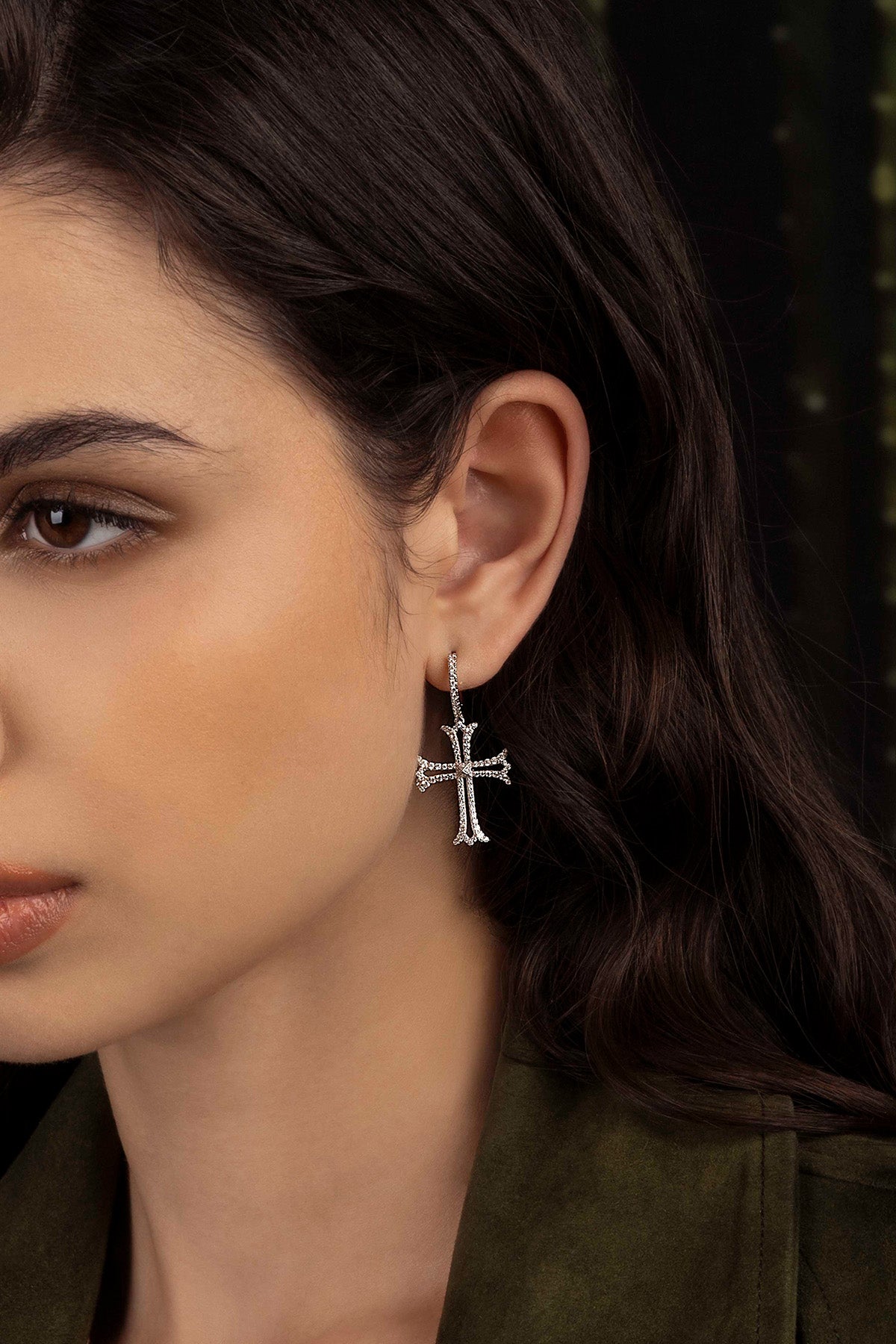 Close-up of a woman wearing a silver cross earring with a blurred background