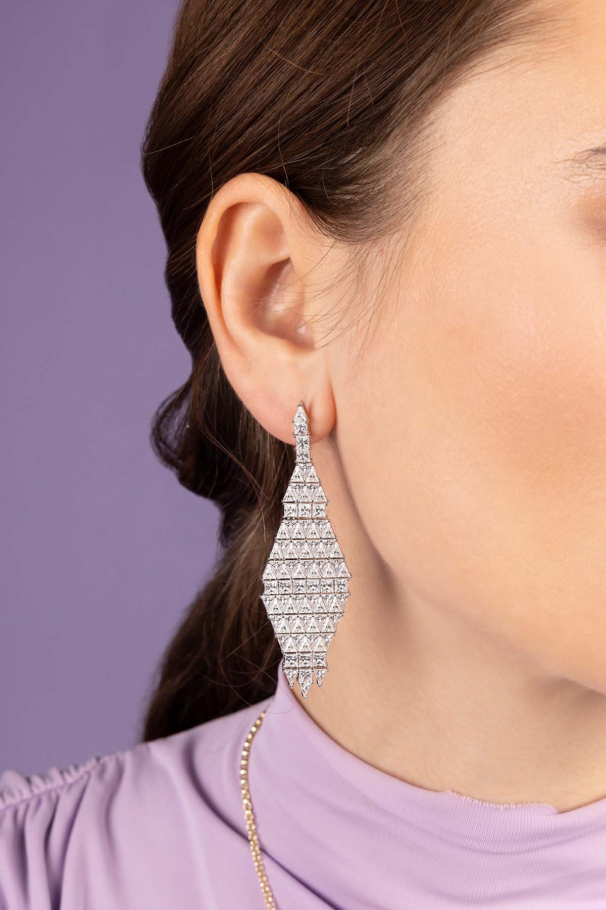 Close-up of a person wearing zirconia earrings with a purple background
