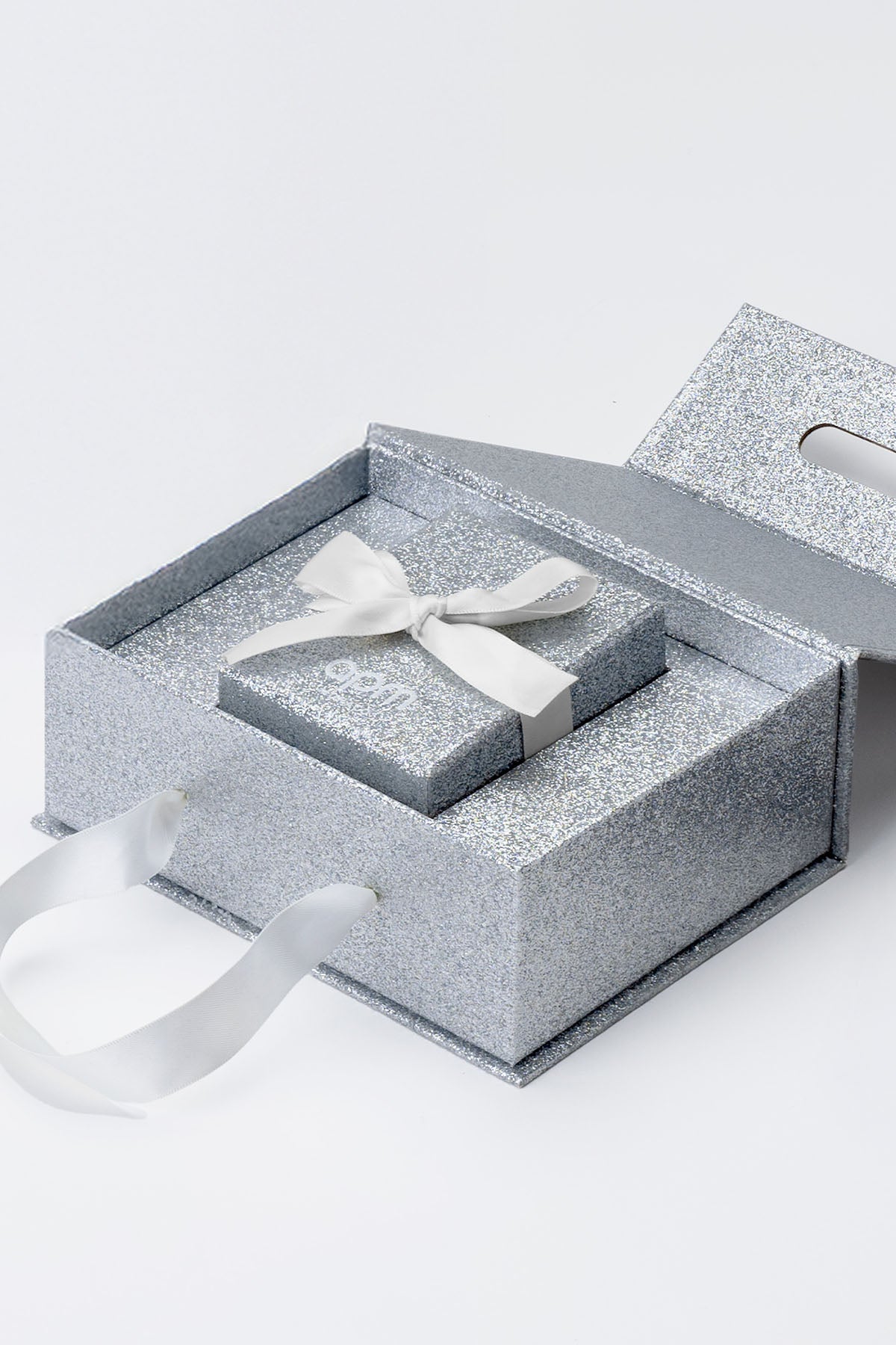 APM Monaco limited edition packaging: Silver jewelry box with a white bow on a white background