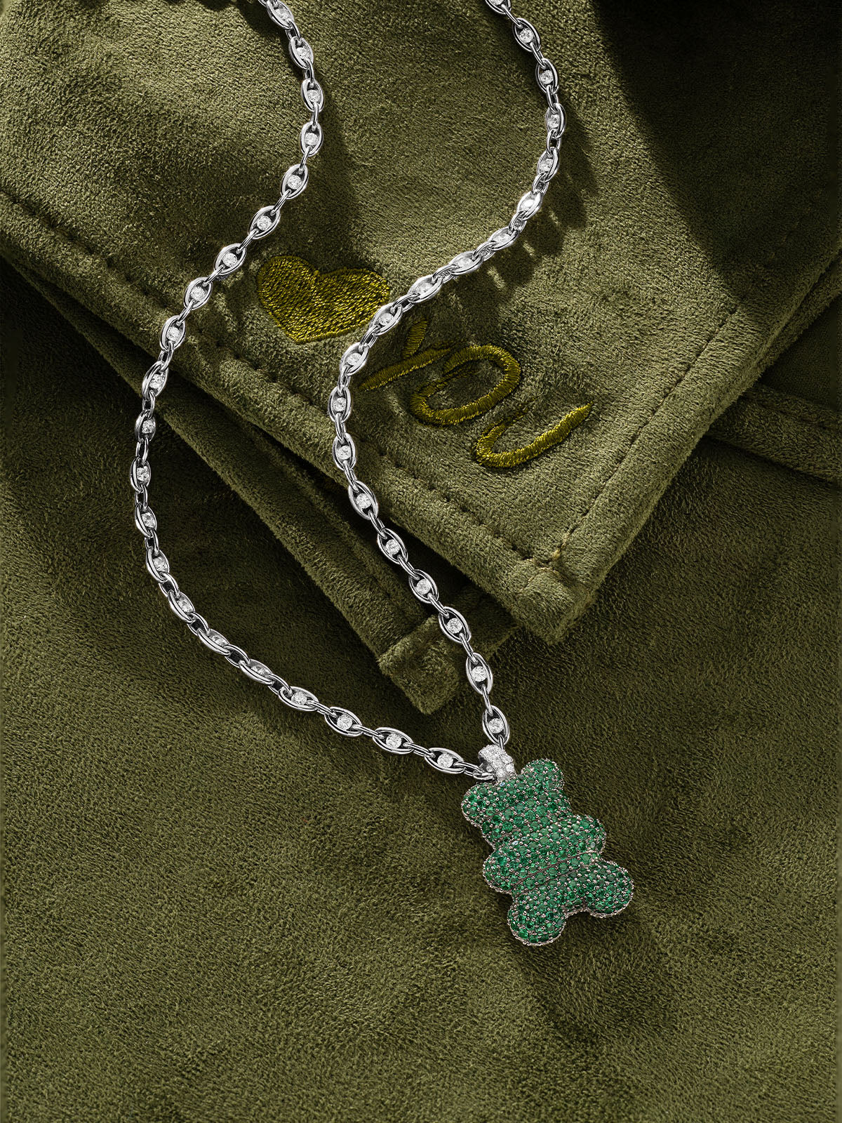 APM MONACO silver necklace with a green yummy bear on a green fabric background