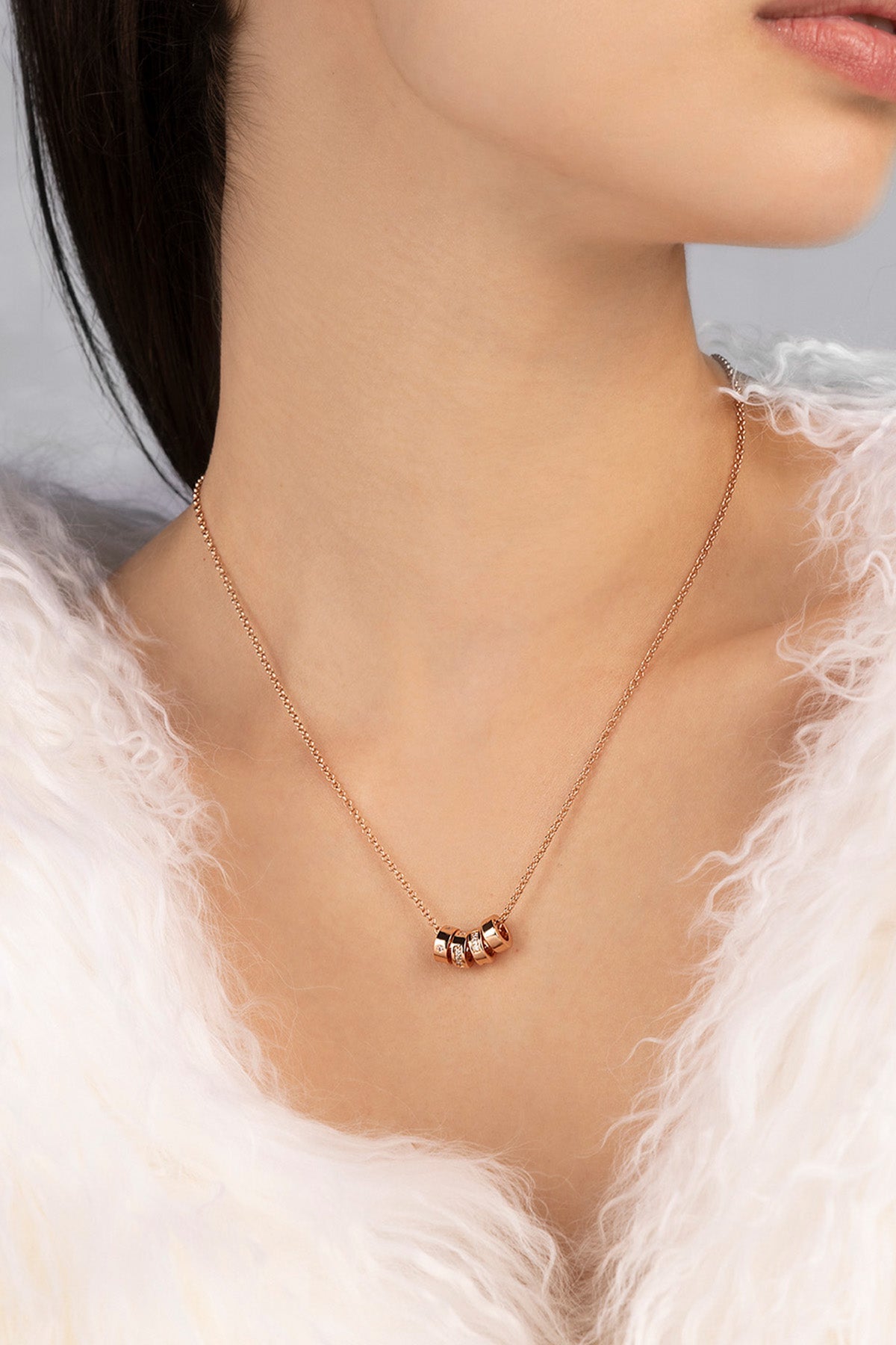 Rose gold necklace with small beads on a model wearing a white fur coat.