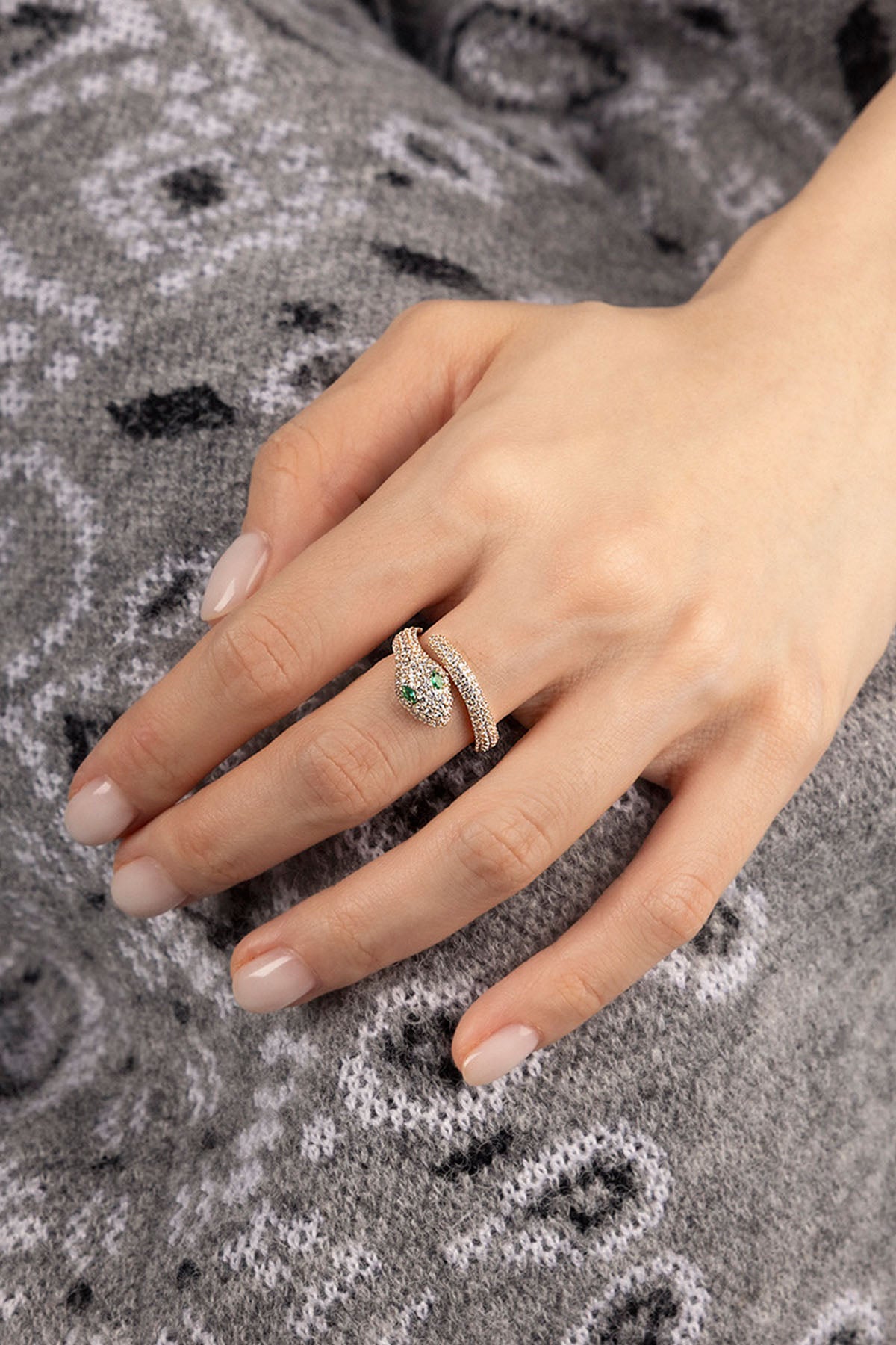 Hand wearing a ring with white and green stones on a textured gray fabric background