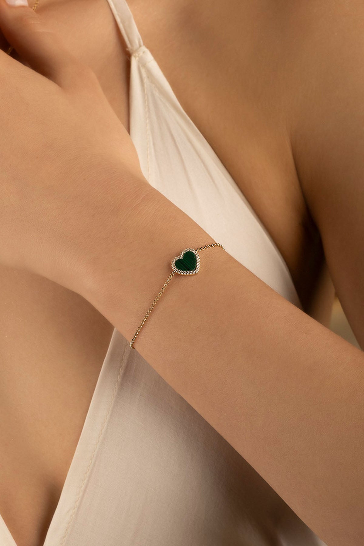 Close-up of a person wearing a gold bracelet with a green heart charm