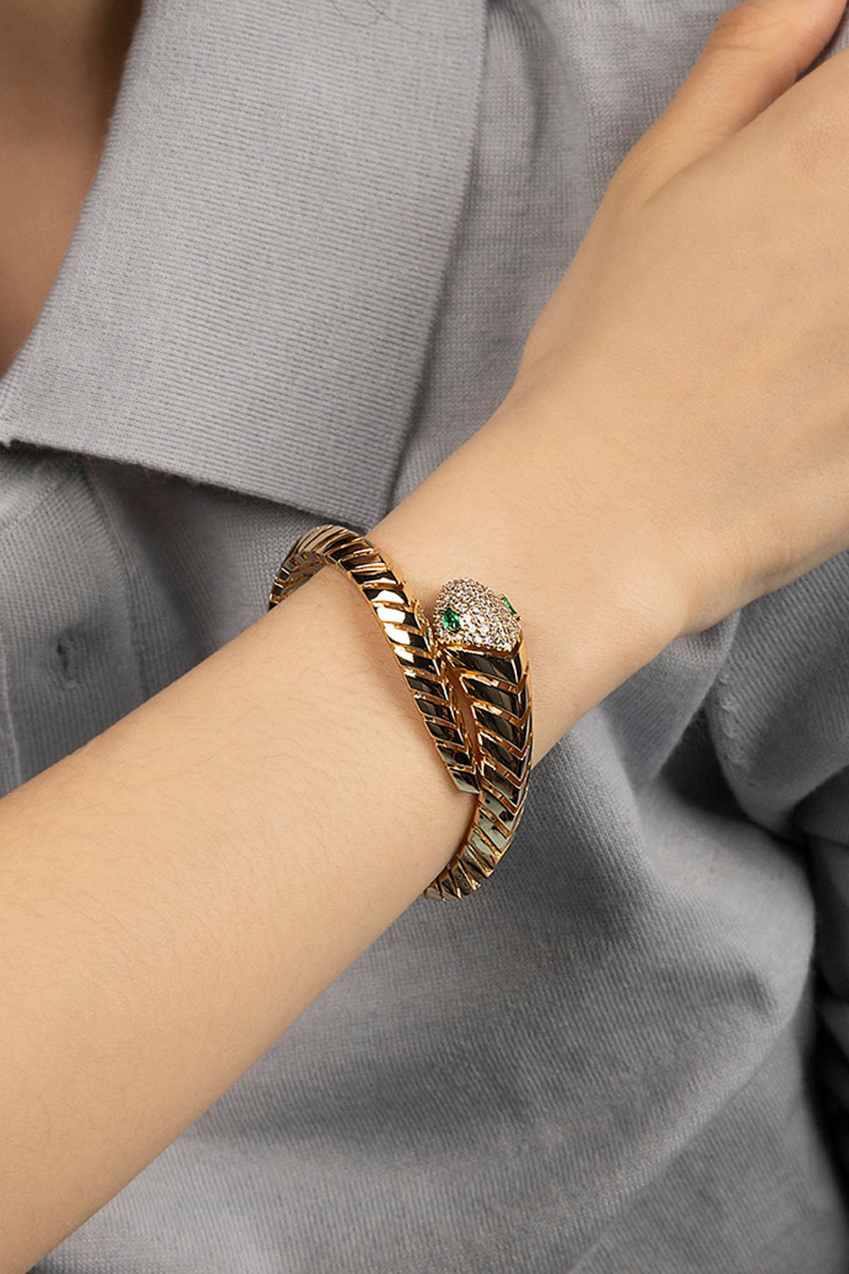 Gold bracelet with green gemstone on a wrist against a gray background
