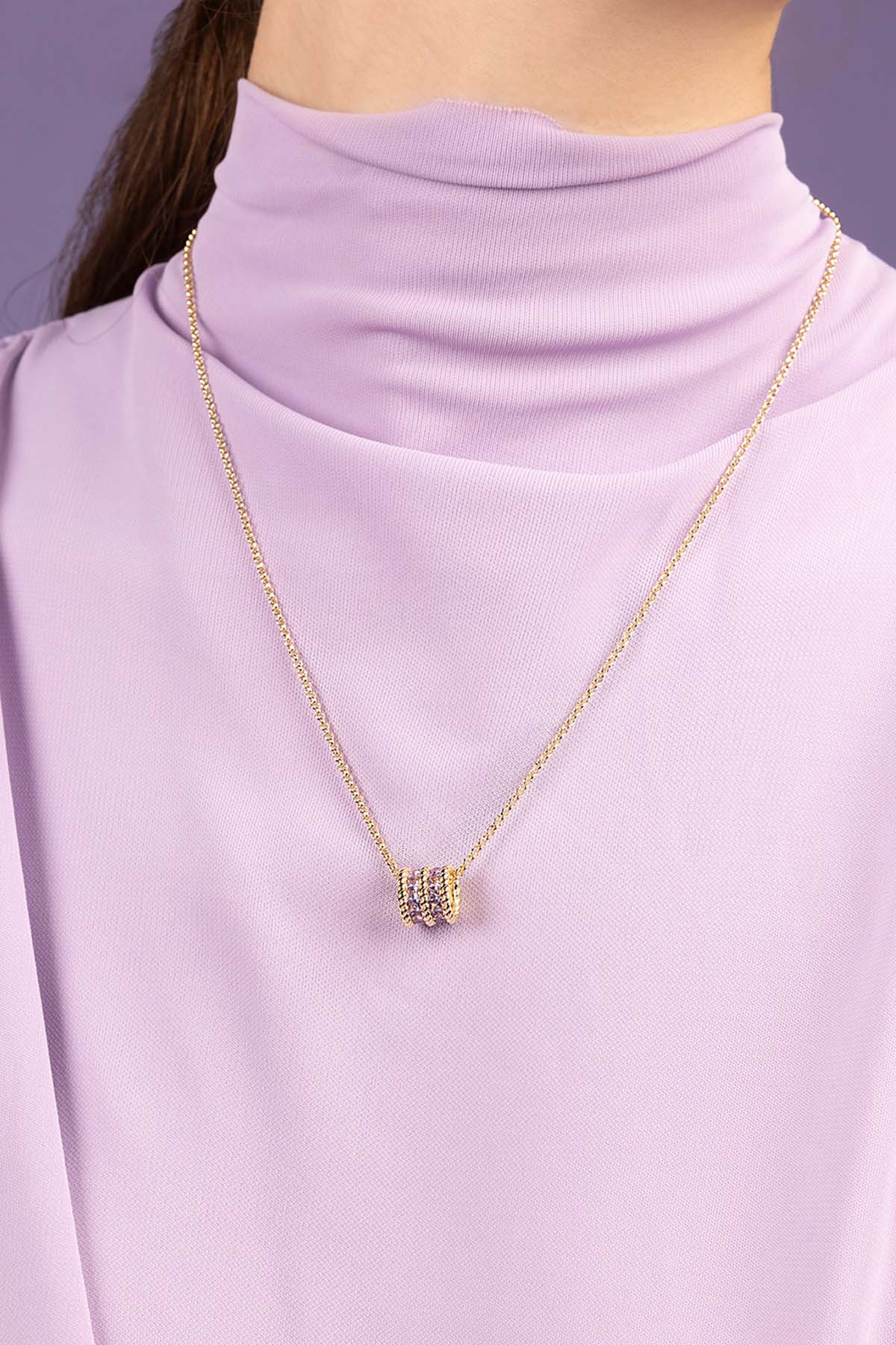 Gold necklace with a pendant on a person wearing a light purple turtleneck.